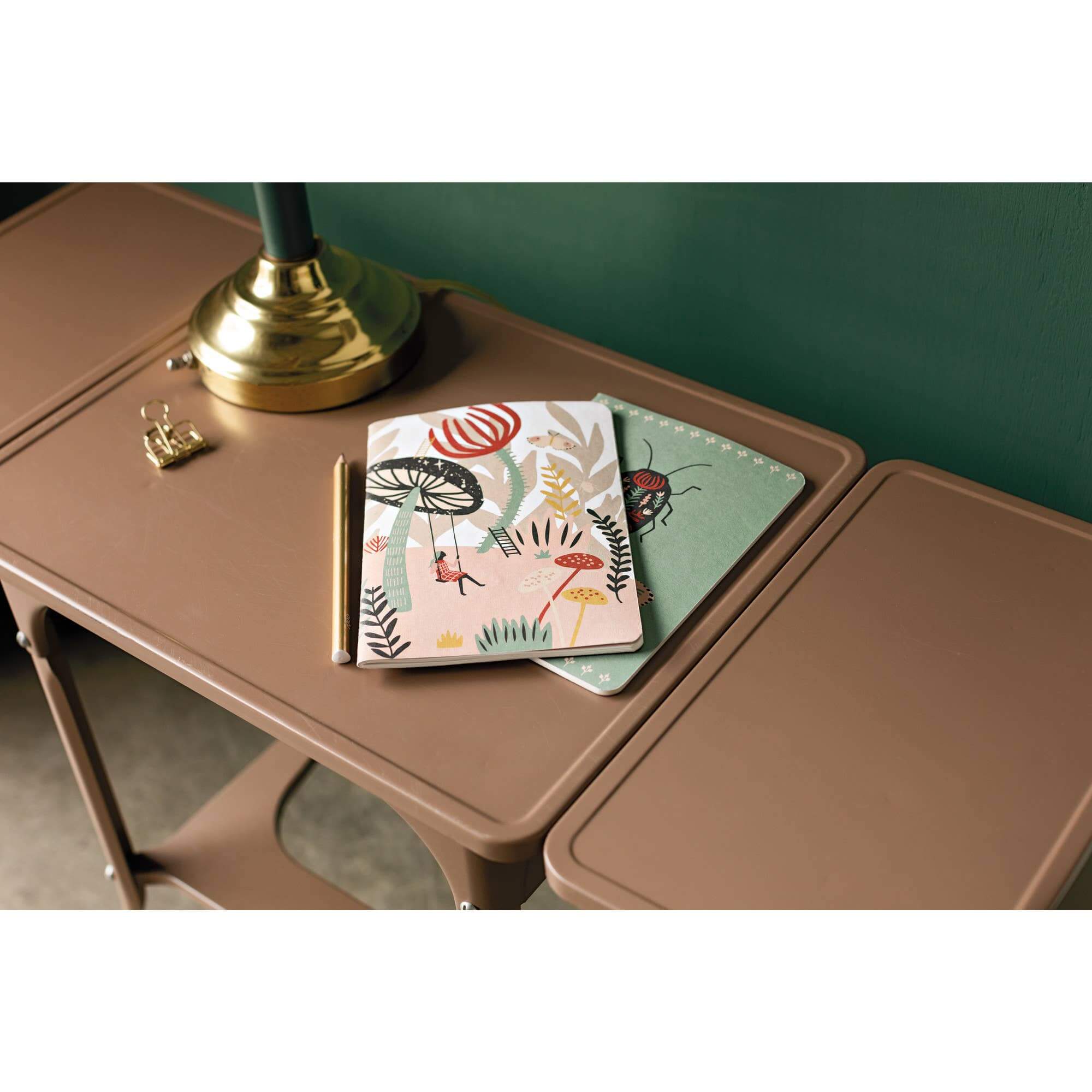 Danica Studio Far And Away Notebook set of 2 with colorful designs on a brown table, featuring a lamp and decorative items.