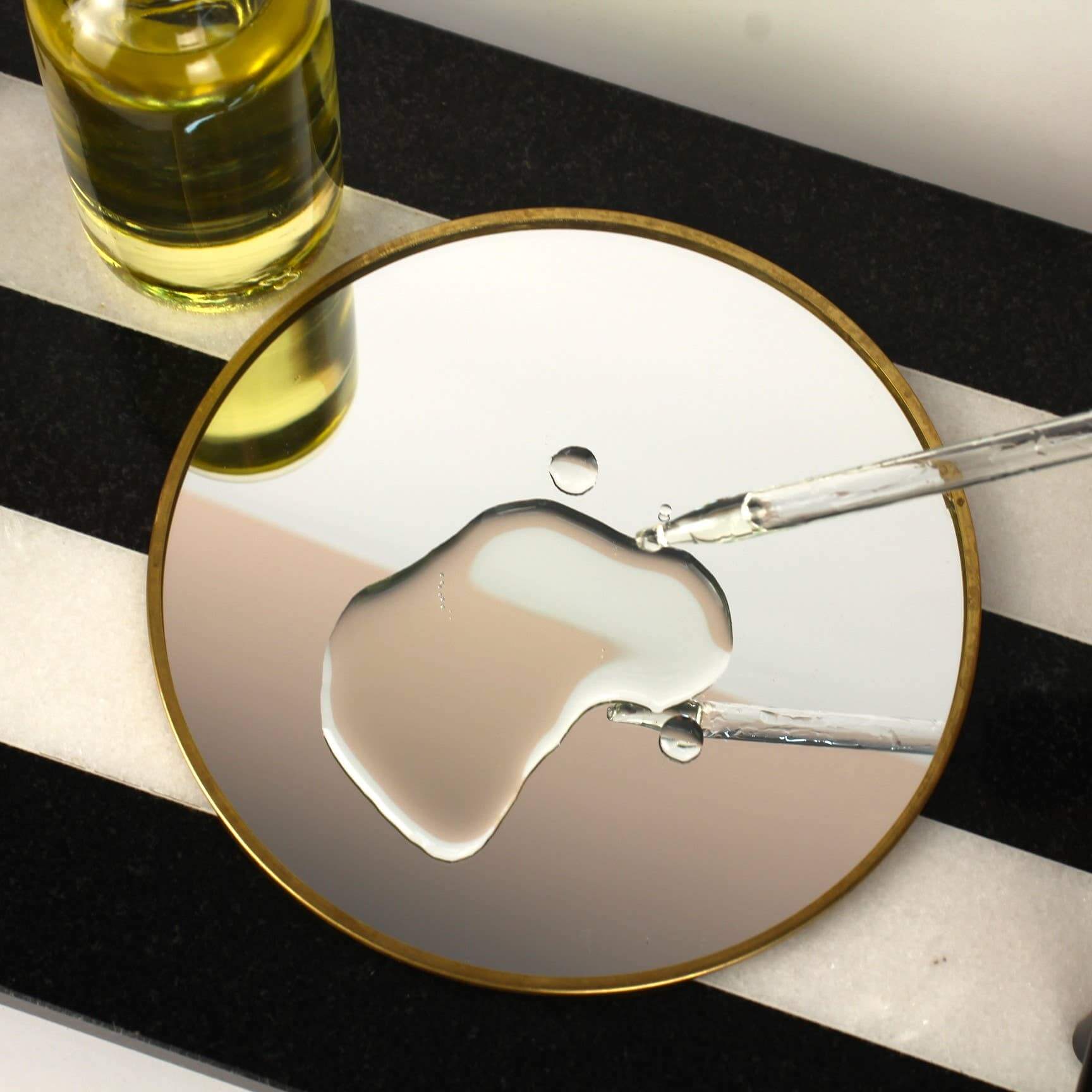 Close-up of luxurious bath oil dropper over reflective surface, showcasing the smooth texture of Moscato, Peach + Pineapple oil.