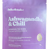 Ashwagandha + Chill herbal tea blend pouch beside a glass of brewed tea and fresh flowers.