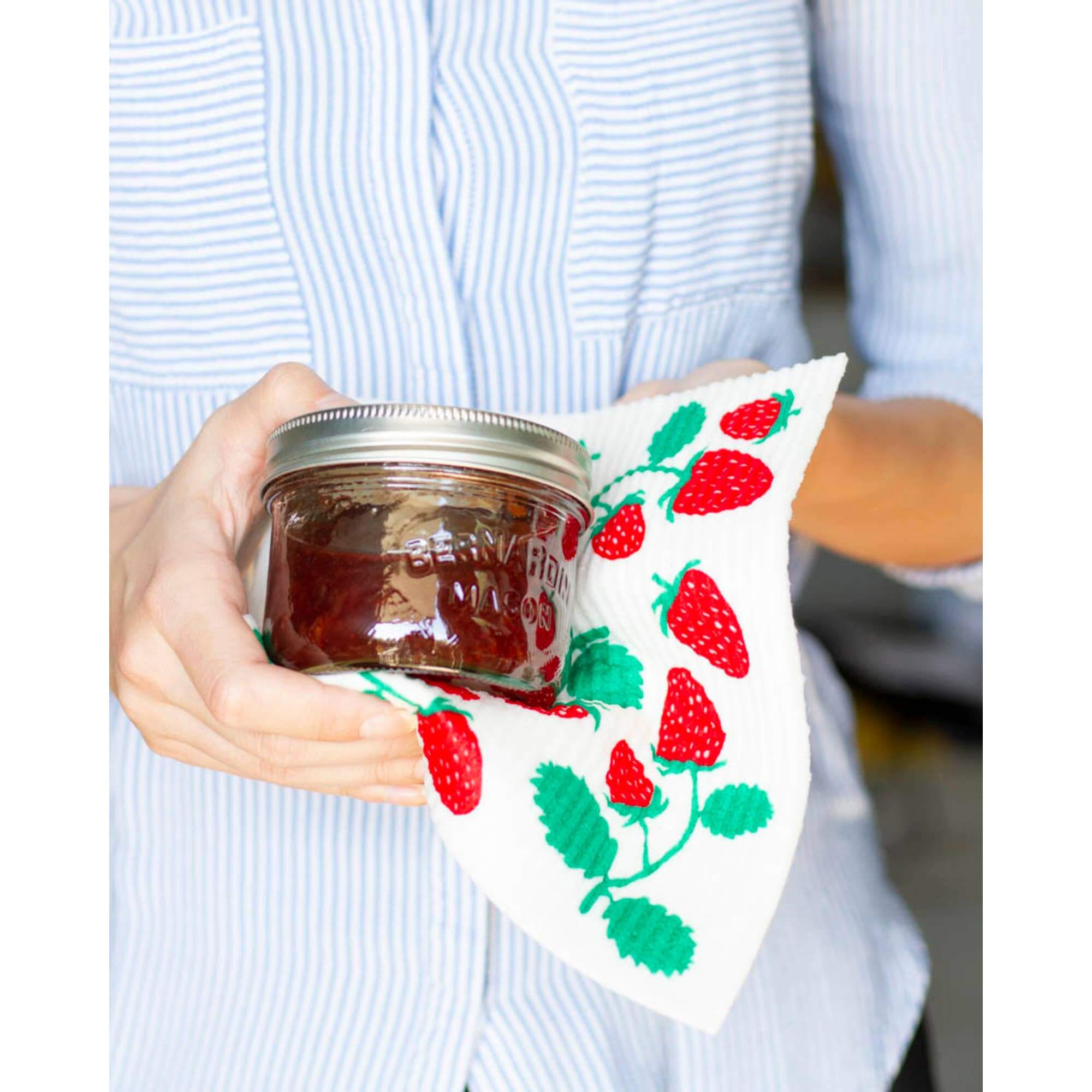 Person holding jar with Swedish dishcloth featuring strawberries, showcasing its versatility in cleaning.