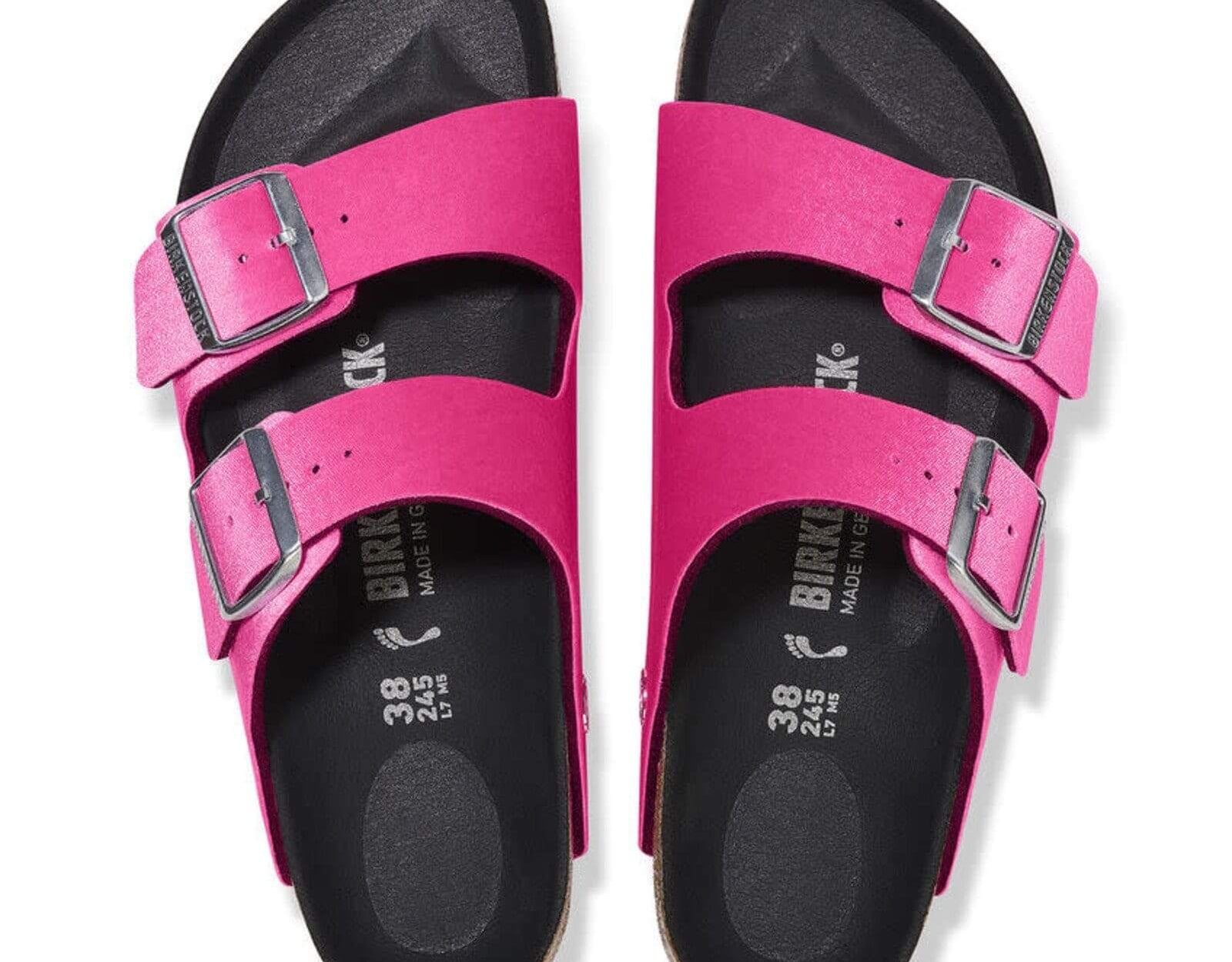 Birkenstock Women's Arizona Sandals in bright pink with rivet buckles and smooth black footbed, top view.