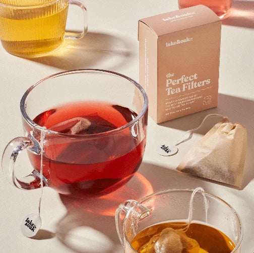 A glass tea cup fill with the ruby red color of Lake and Oak Superberry immunity tea with a box of Perfect Tea filters to the side