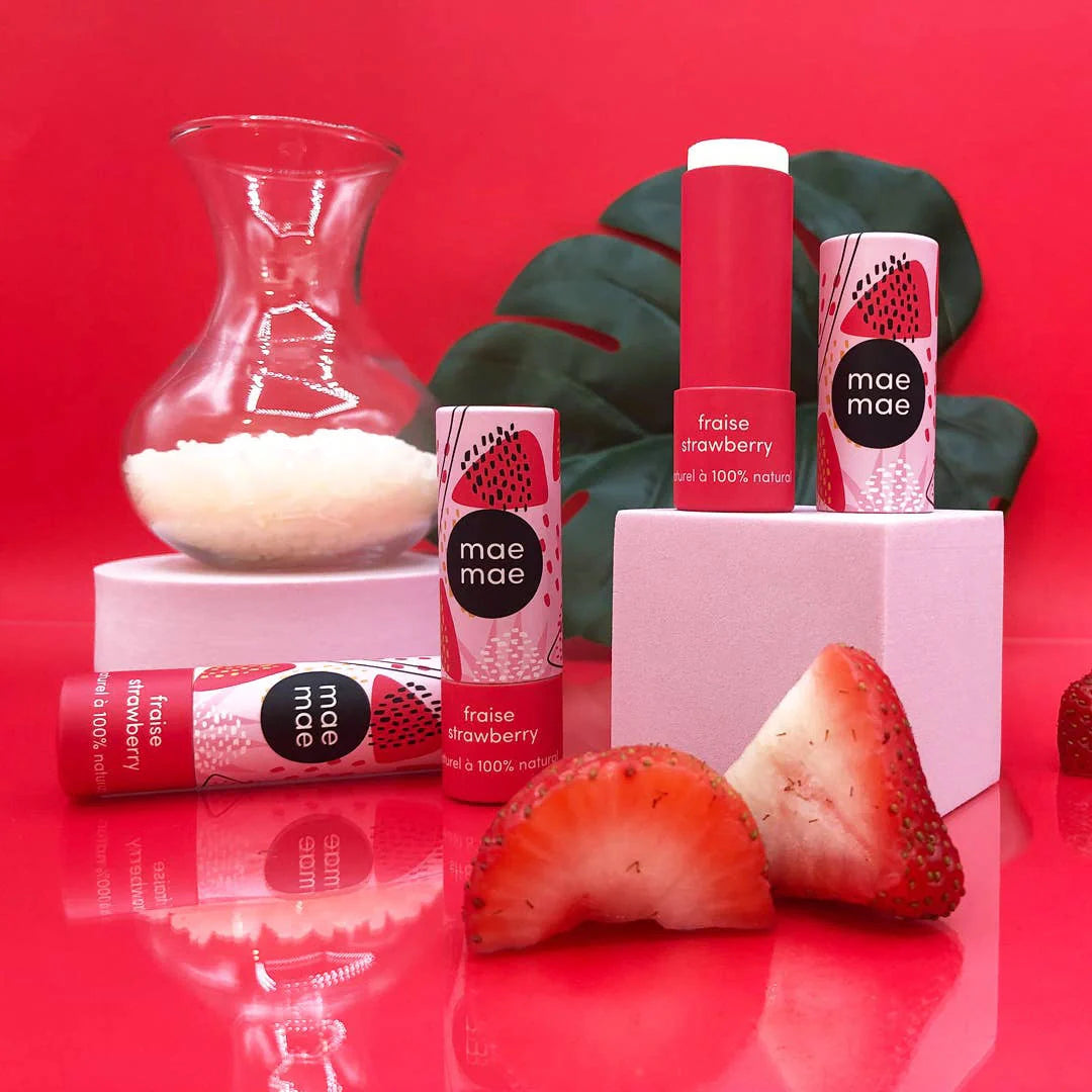 MaeMae strawberry lip balms on a red background with fresh red strawberries, using sustainable cardboard tube packaging