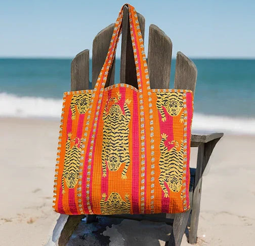 A richly patterned red and orange artisan cotton tote bag hanging from a post at the beach
