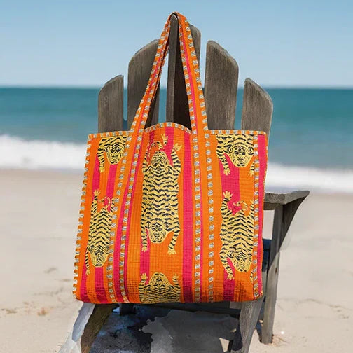 A richly patterned red and orange artisan cotton tote bag hanging from a post at the beach