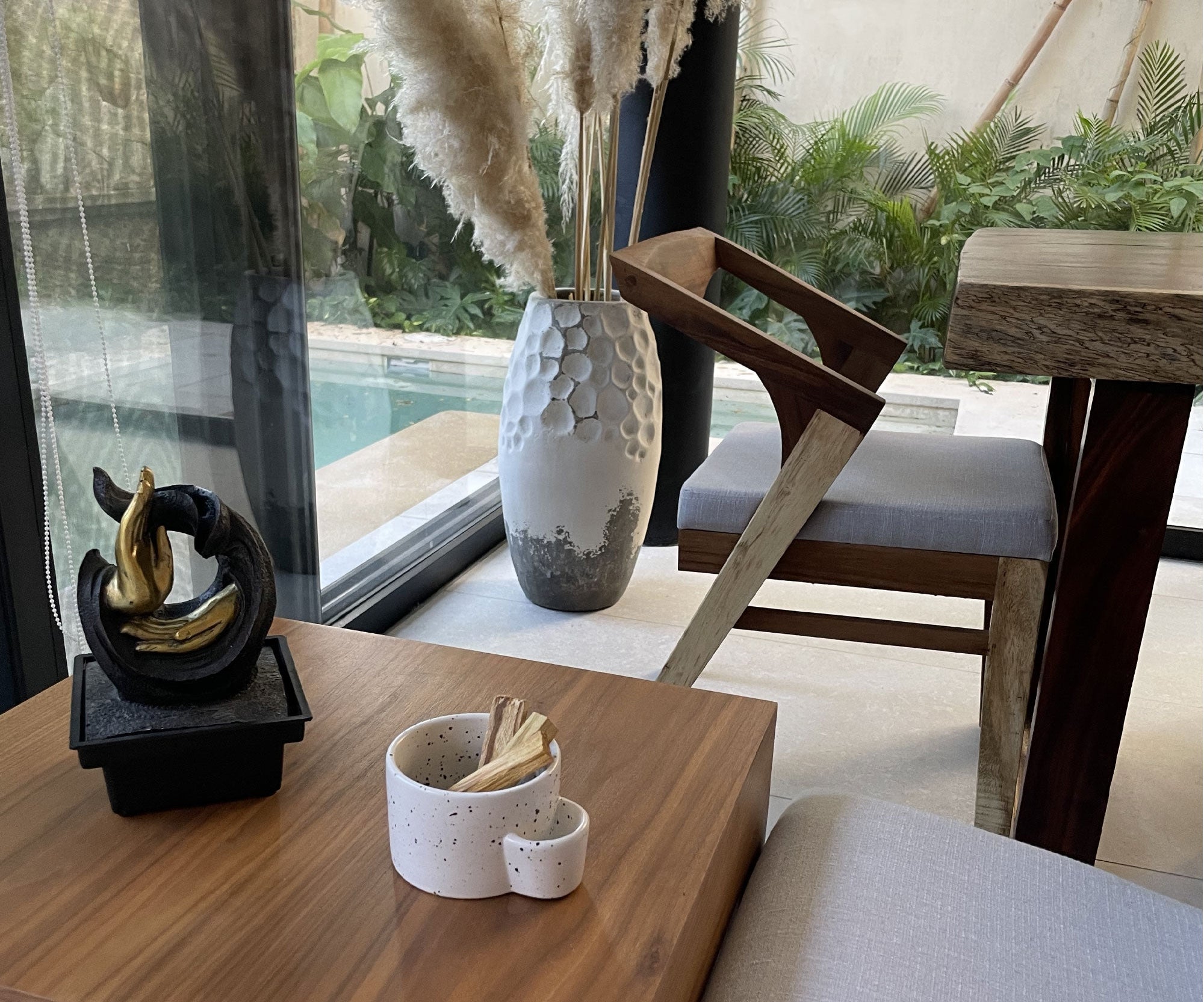 Decorative elements on a wooden table with a view of a pool and outdoor furniture.