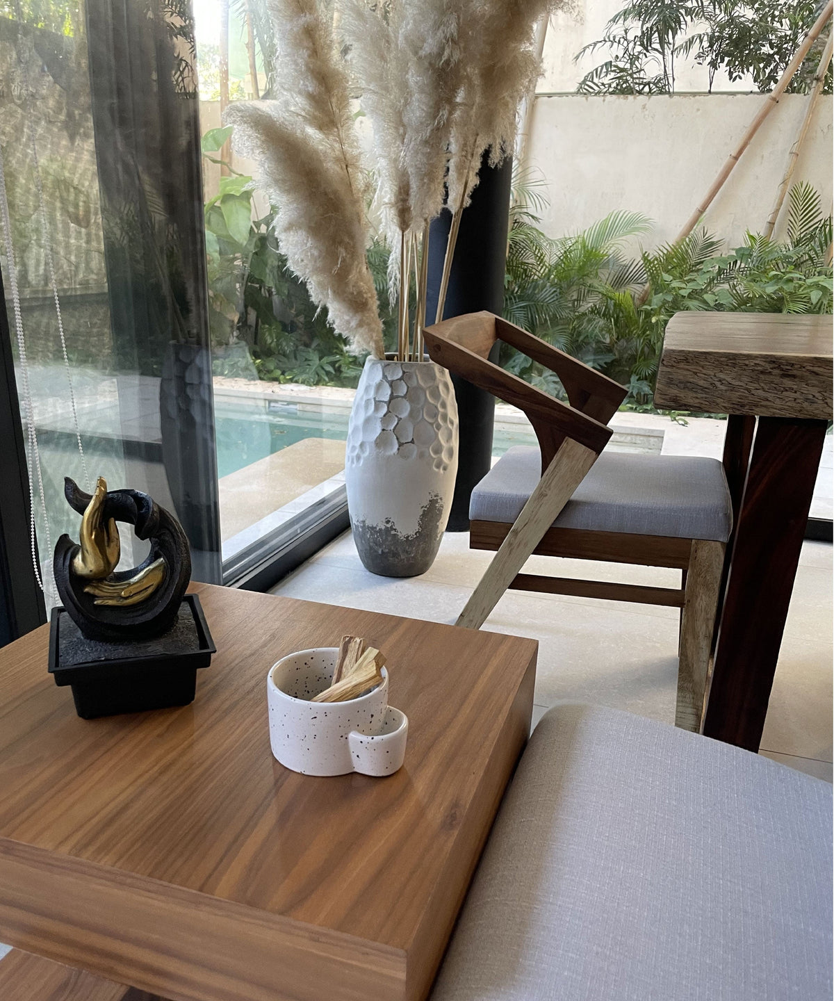 Decorative elements on a wooden table with a view of a pool and outdoor furniture.