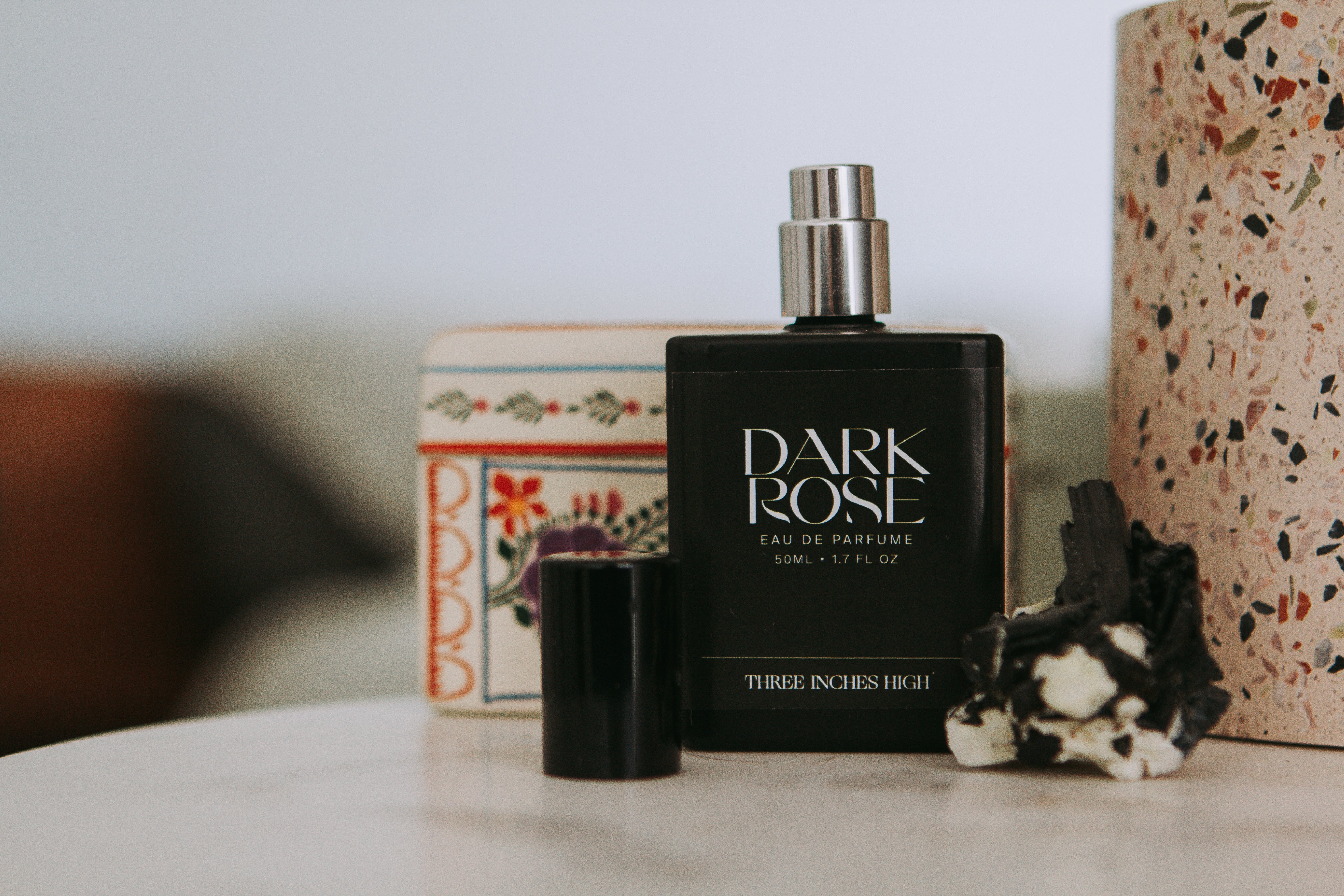 Dark Rose eau de parfum bottle on a surface with decorative items in the background