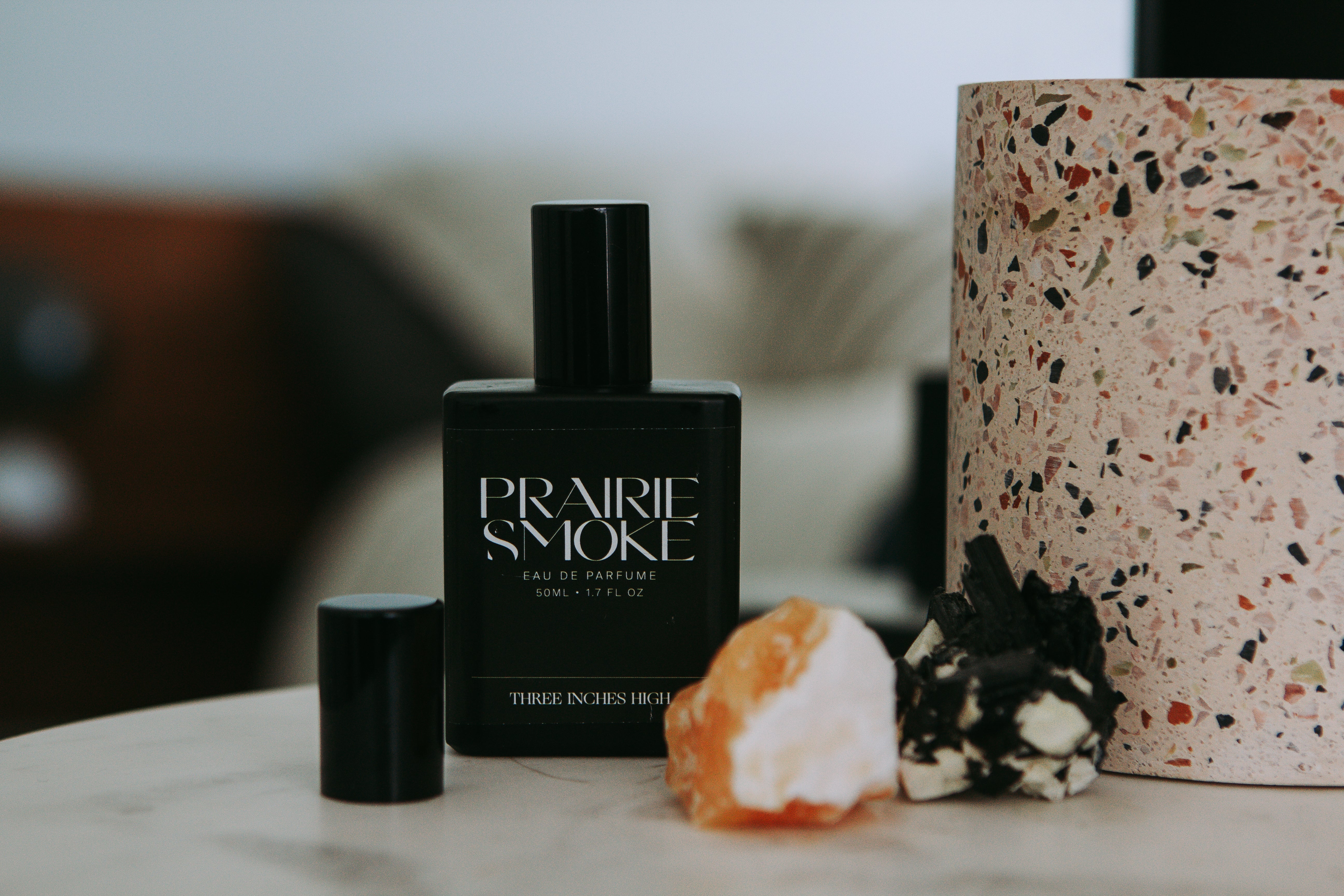 Perfume bottle labeled 'Prairie Smoke' on a surface with decorative items.