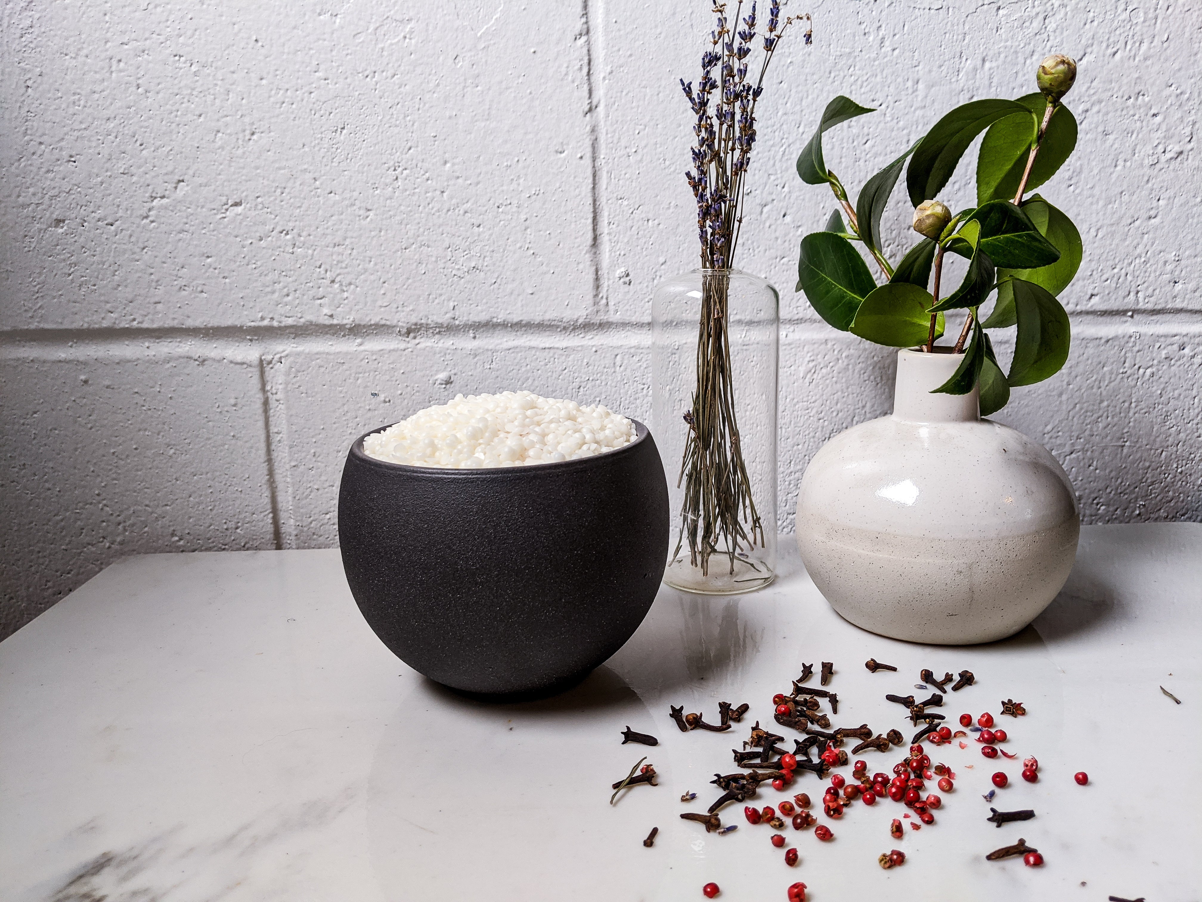 Black bowl with white rice, white vase with green leaves, and small glass container on a white surface.
