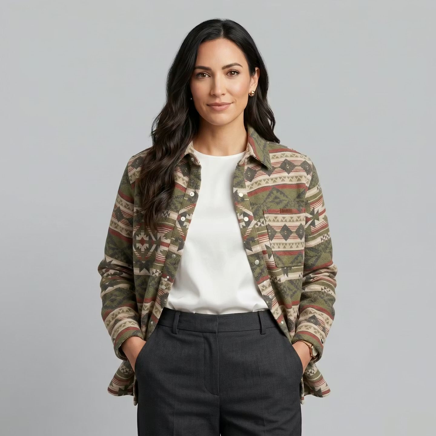 OldTribes Woman wearing a patterned jacket over a white shirt and dark pants on a grey background
