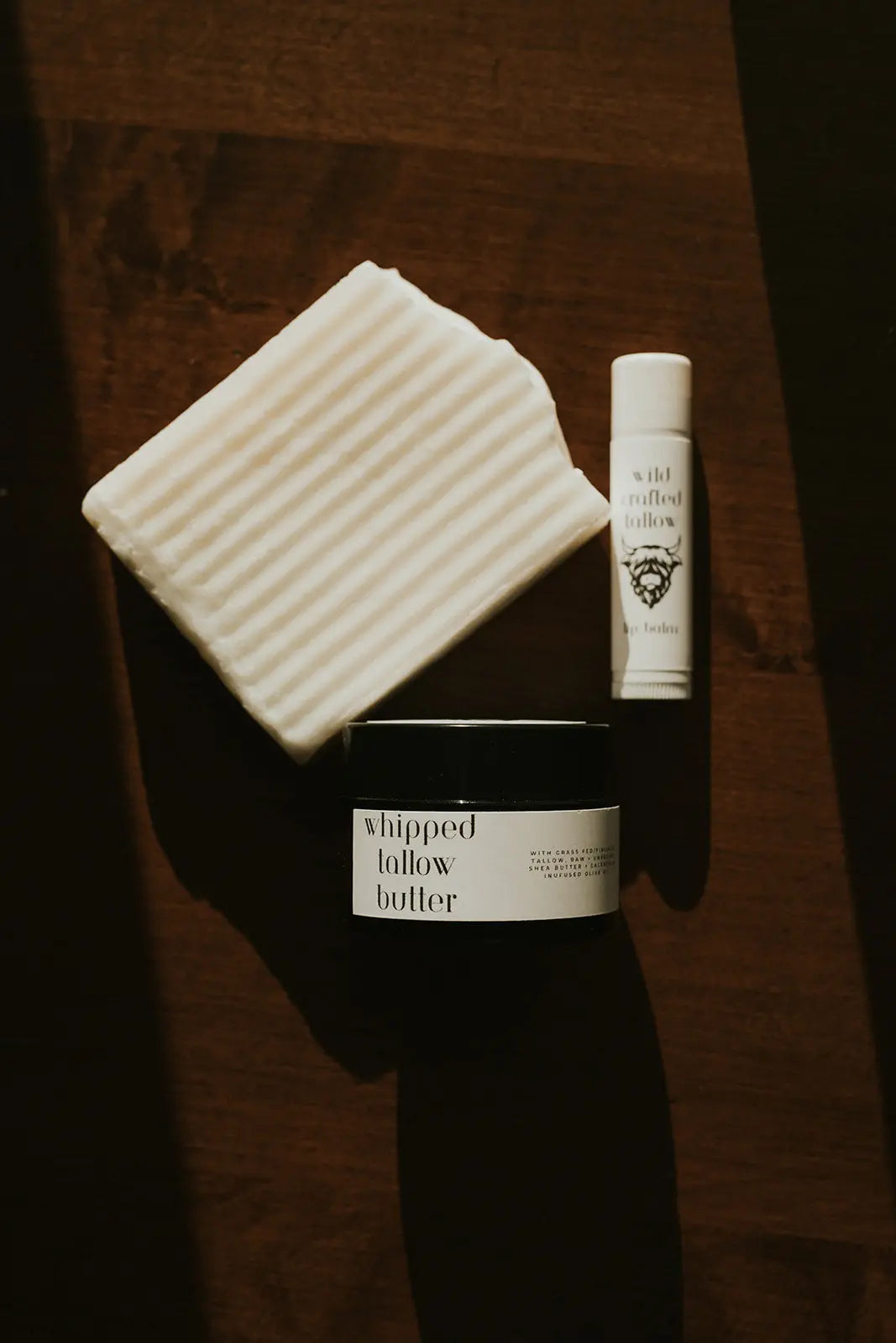 Three skincare products on a wooden surface: a jar, a bottle, and a soap bar.