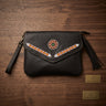 Black leather clutch bag with hand-beaded geometric details and a tassel, displayed on a dark wood background 