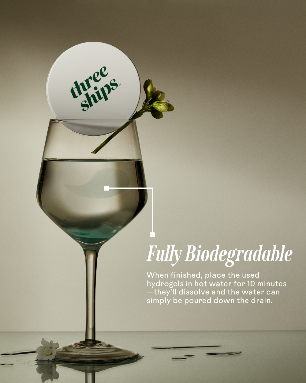 A biodegradable eye mask in a glass of water with a flower, showcasing its eco-friendly properties.