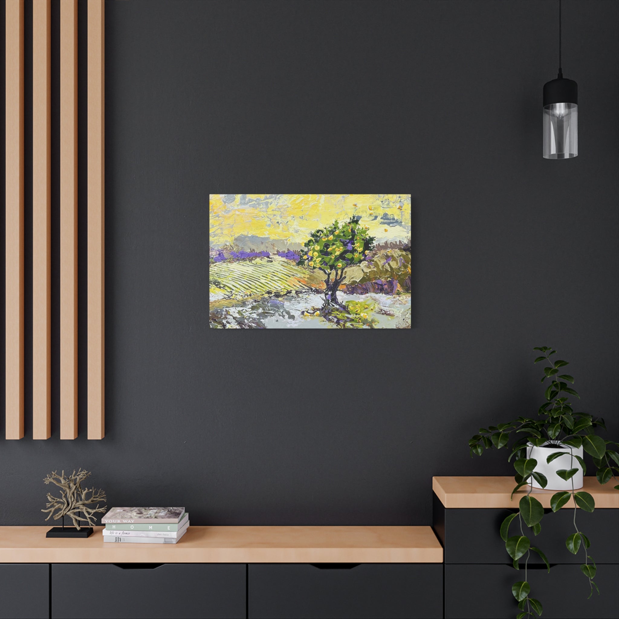A small landscape painting of a tree in a field, displayed on a dark gray wall above a light wood console table in a modern room setting.