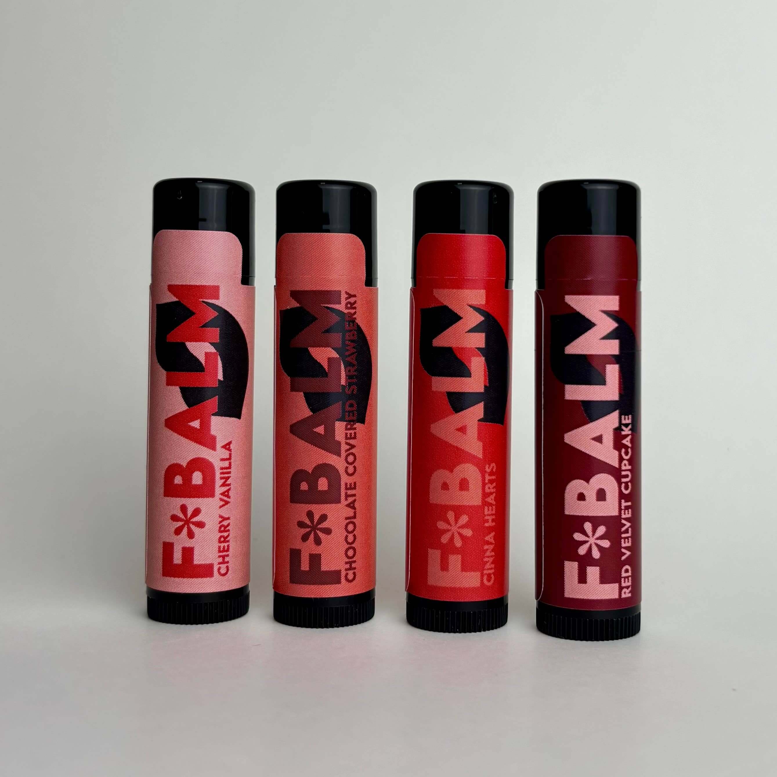 Four lip balms in tube packaging: Cherry Vanilla, Chocolate Covered Strawberry, Cinna Hearts, and Red Velvet Cupcake.