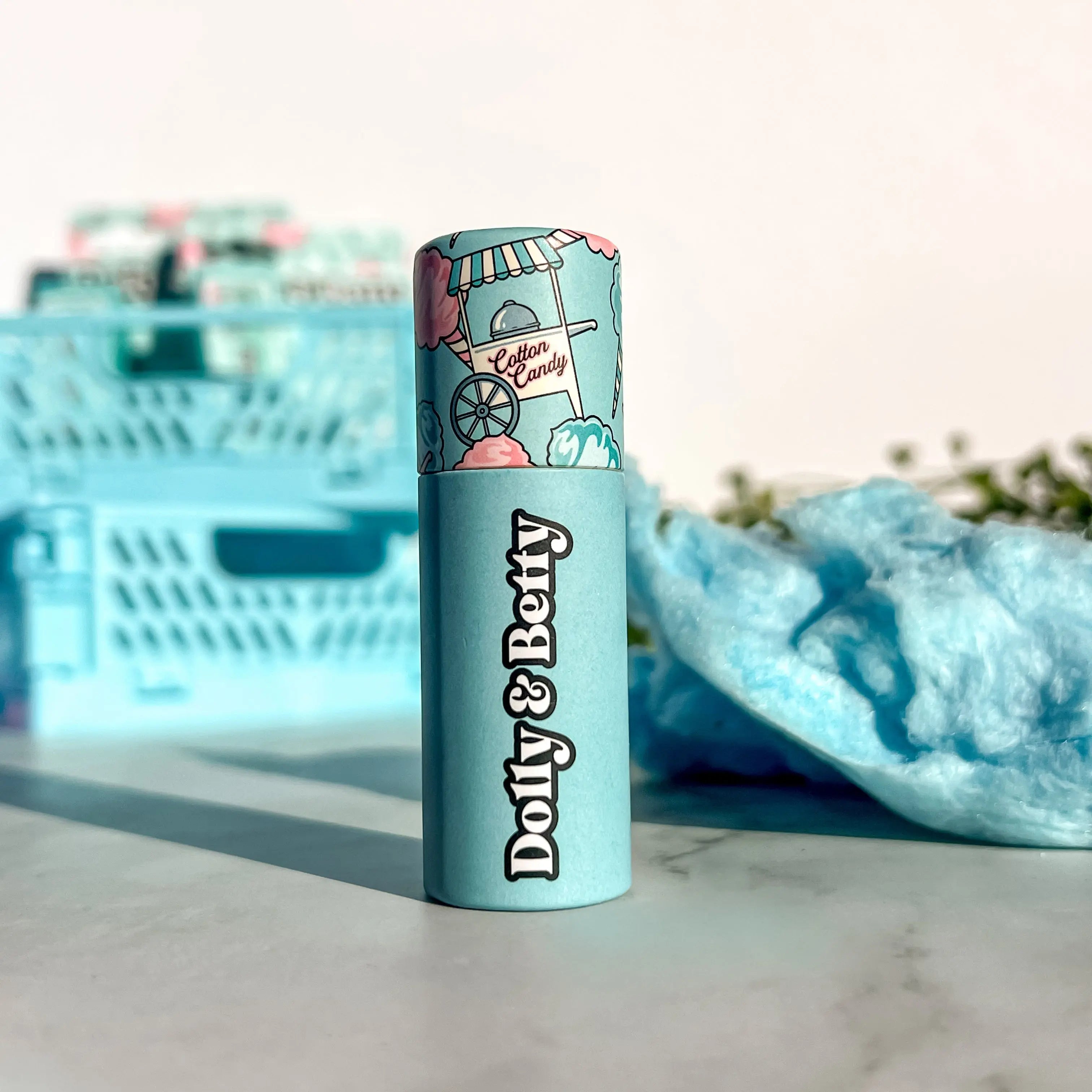Lip balm with 'Dolly & Betty' branding on a marble surface with cotton candy-themed packaging.