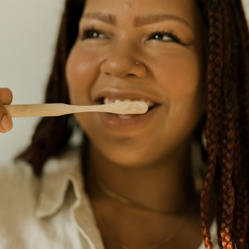 Woman holding a wooden spoon with a white substance, possibly toothpaste, against a neutral background.