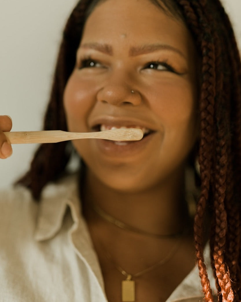 Woman holding a wooden spoon with a white substance, possibly toothpaste, against a neutral background.