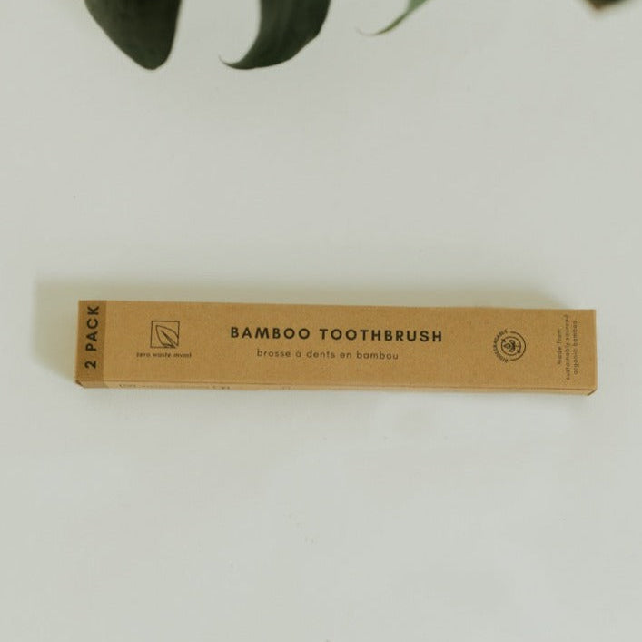 Bamboo toothbrush packaging on a white background with green leaves.