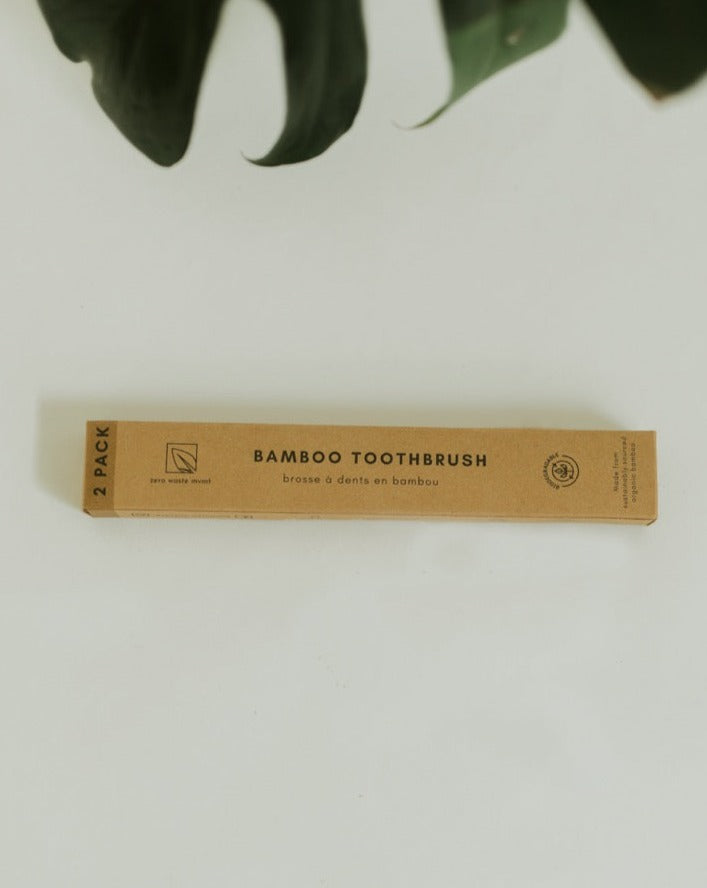 Bamboo toothbrush packaging on a white background with green leaves.