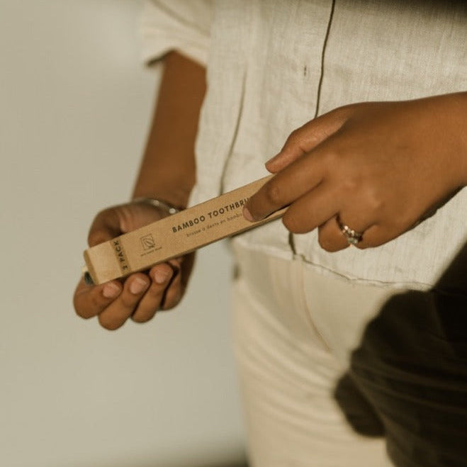 Person holding a bamboo toothbrush packaging with a neutral background