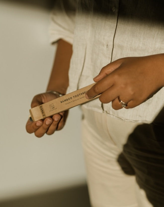 Person holding a bamboo toothbrush packaging with a neutral background