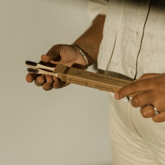 Person holding a set of bamboo toothbrushes with a neutral background