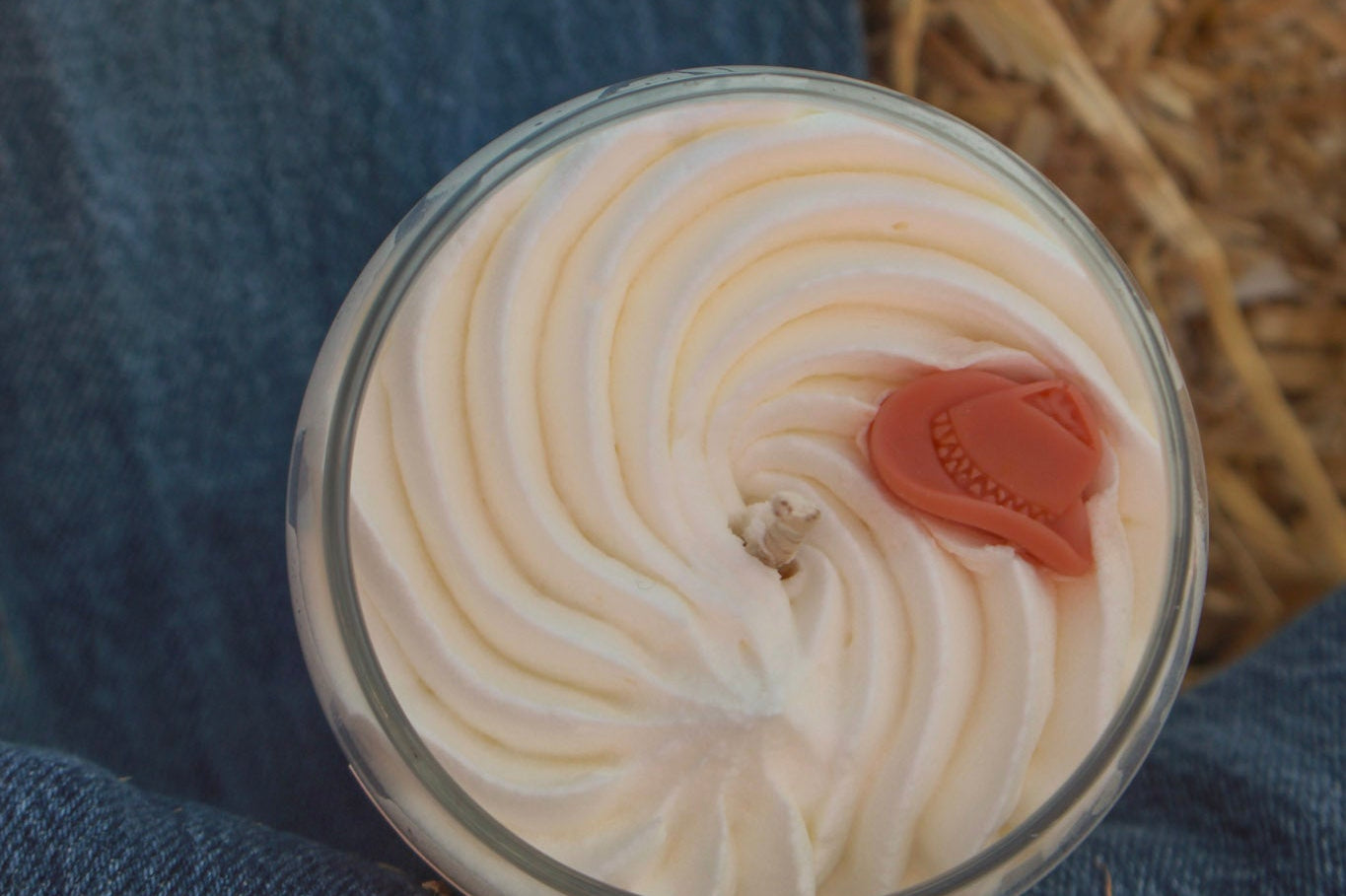 Close-up of a dessert with whipped cream and a cherry on top, placed on a blue fabric surface.