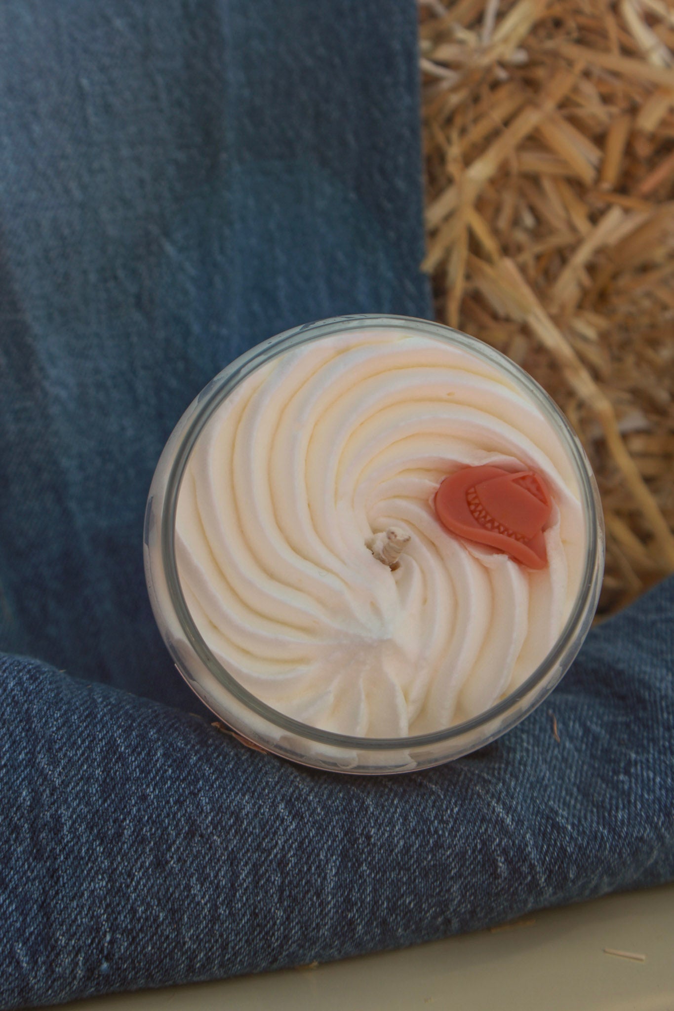 Close-up of a dessert with whipped cream and a cherry on top, placed on a blue fabric surface.