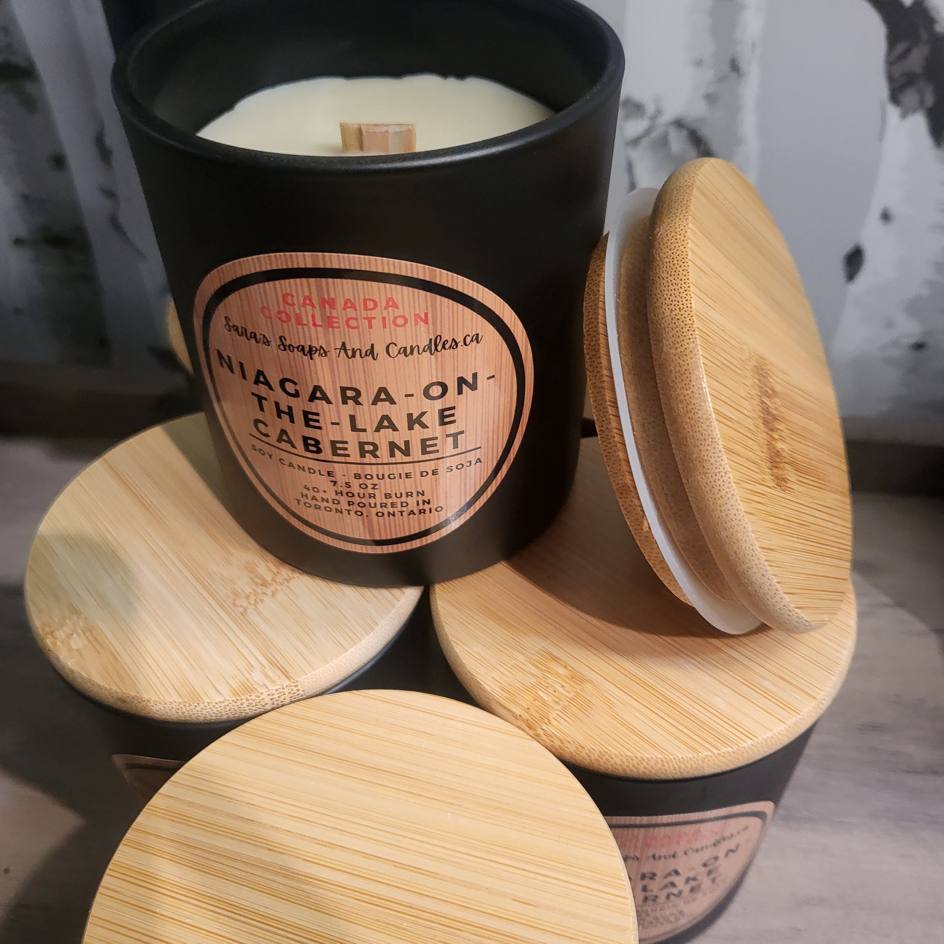 Candle in a black container with wooden lid on a wooden surface