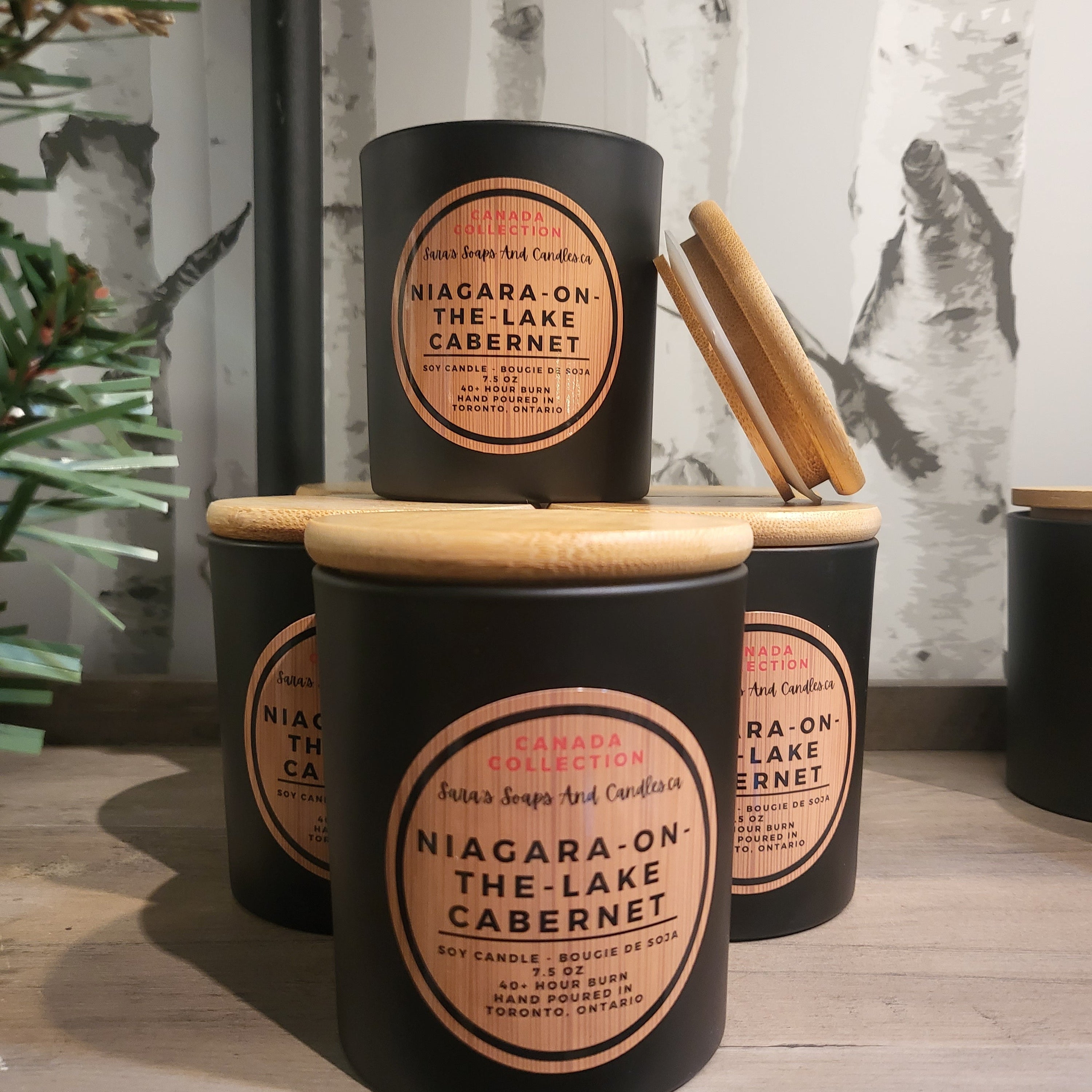 Set of black jars with wooden lids labeled 'Niagara-on-the-Lake Cabernet' on a wooden surface.