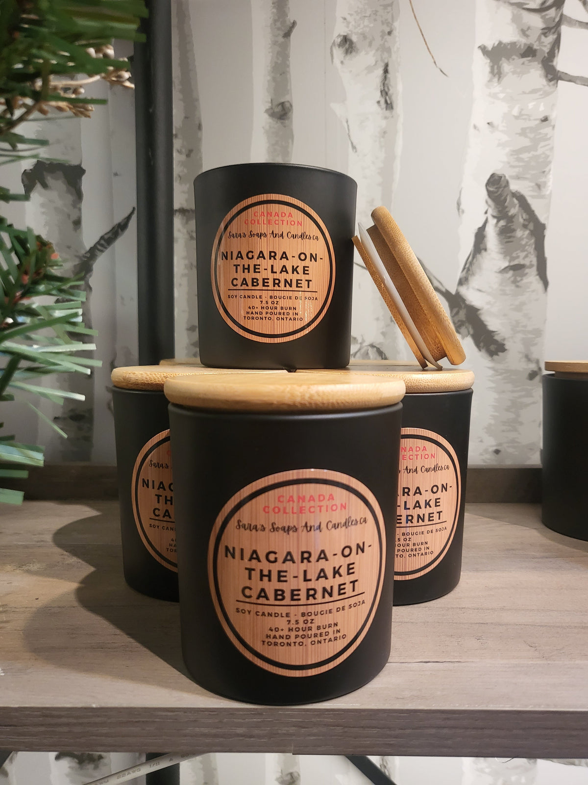 Set of black jars with wooden lids labeled 'Niagara-on-the-Lake Cabernet' on a wooden surface.