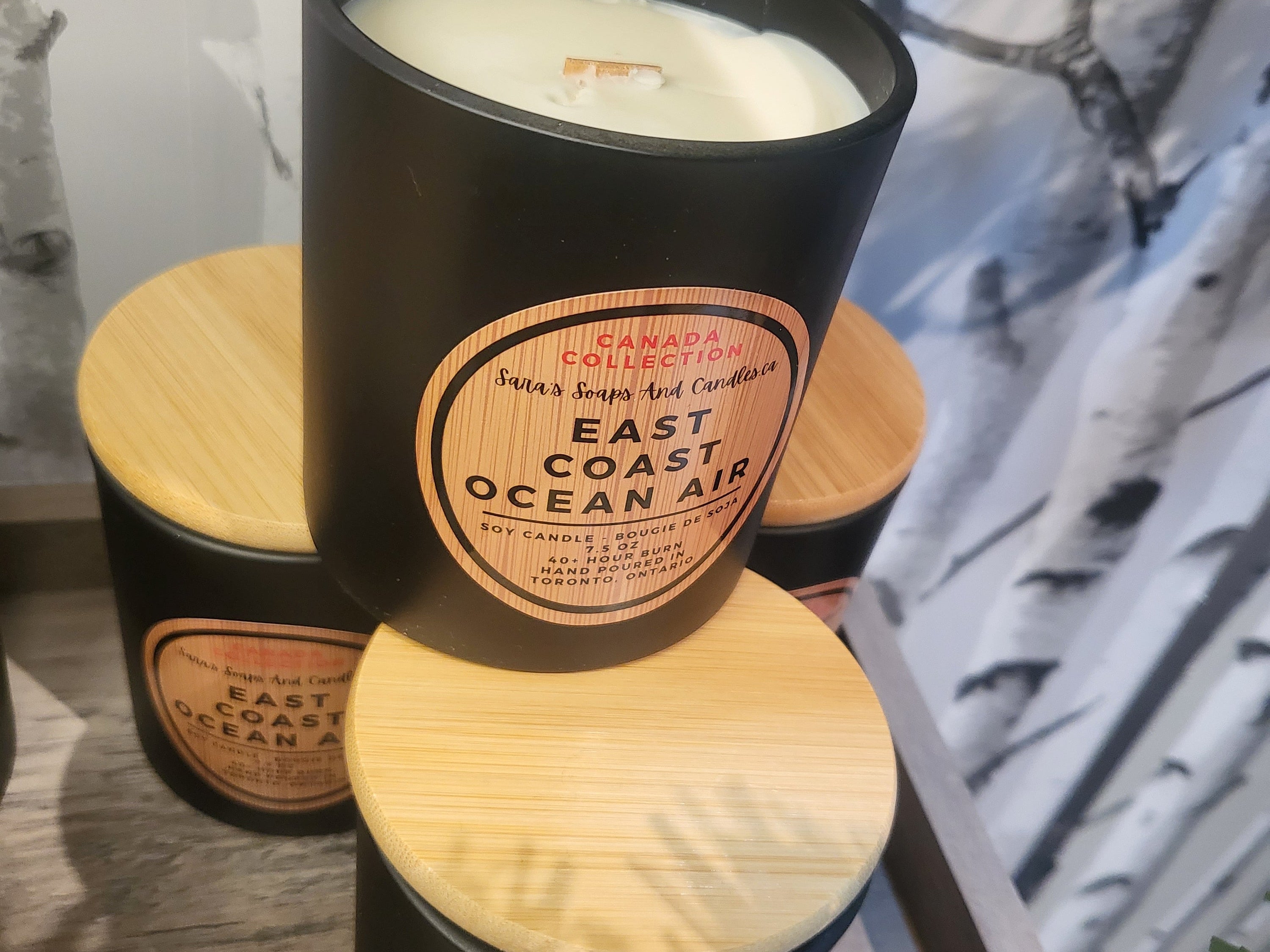Black candle with wooden lid labeled 'East Coast Ocean Air' on a surface.