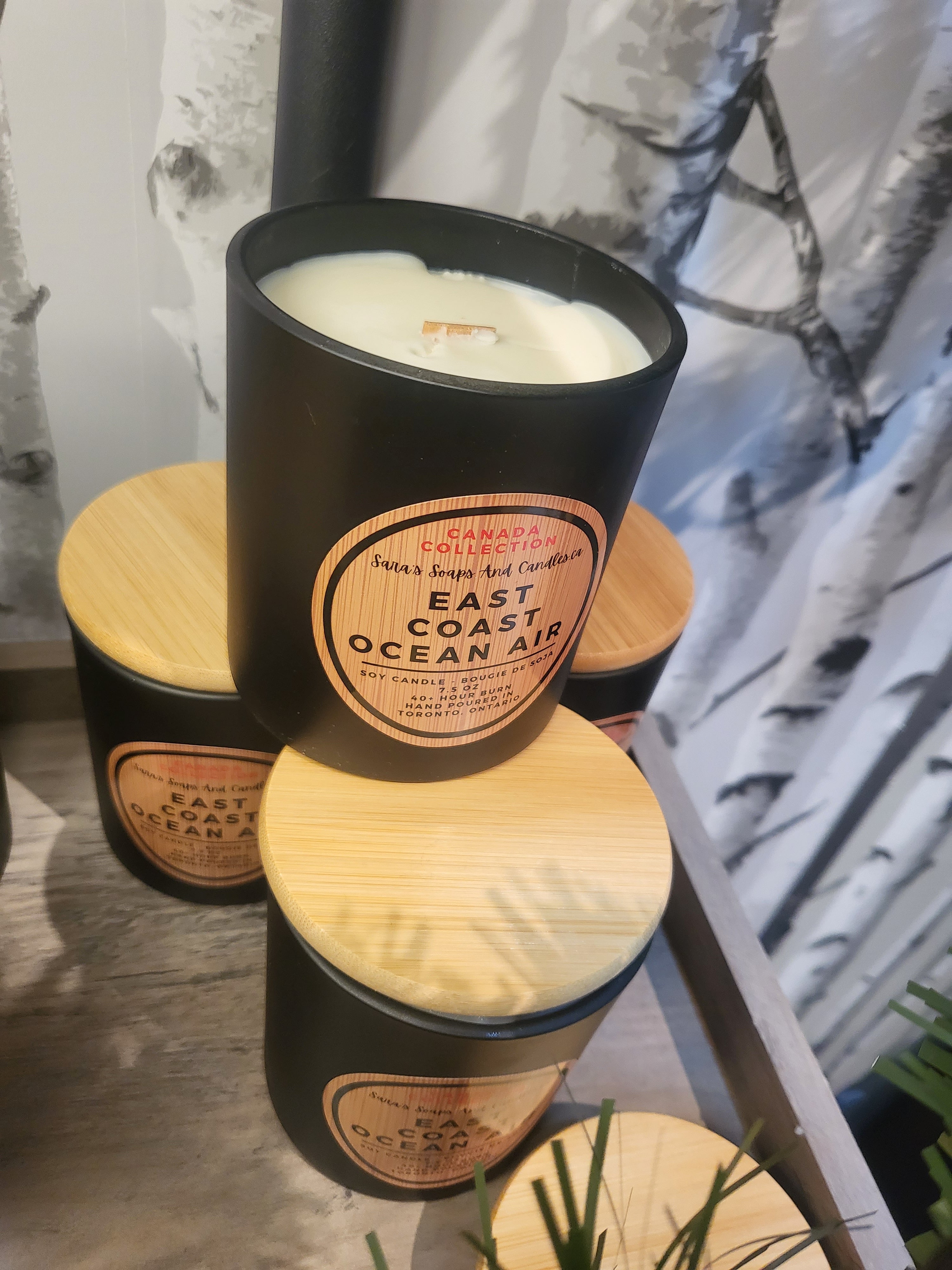 Black candle with wooden lid labeled 'East Coast Ocean Air' on a surface.