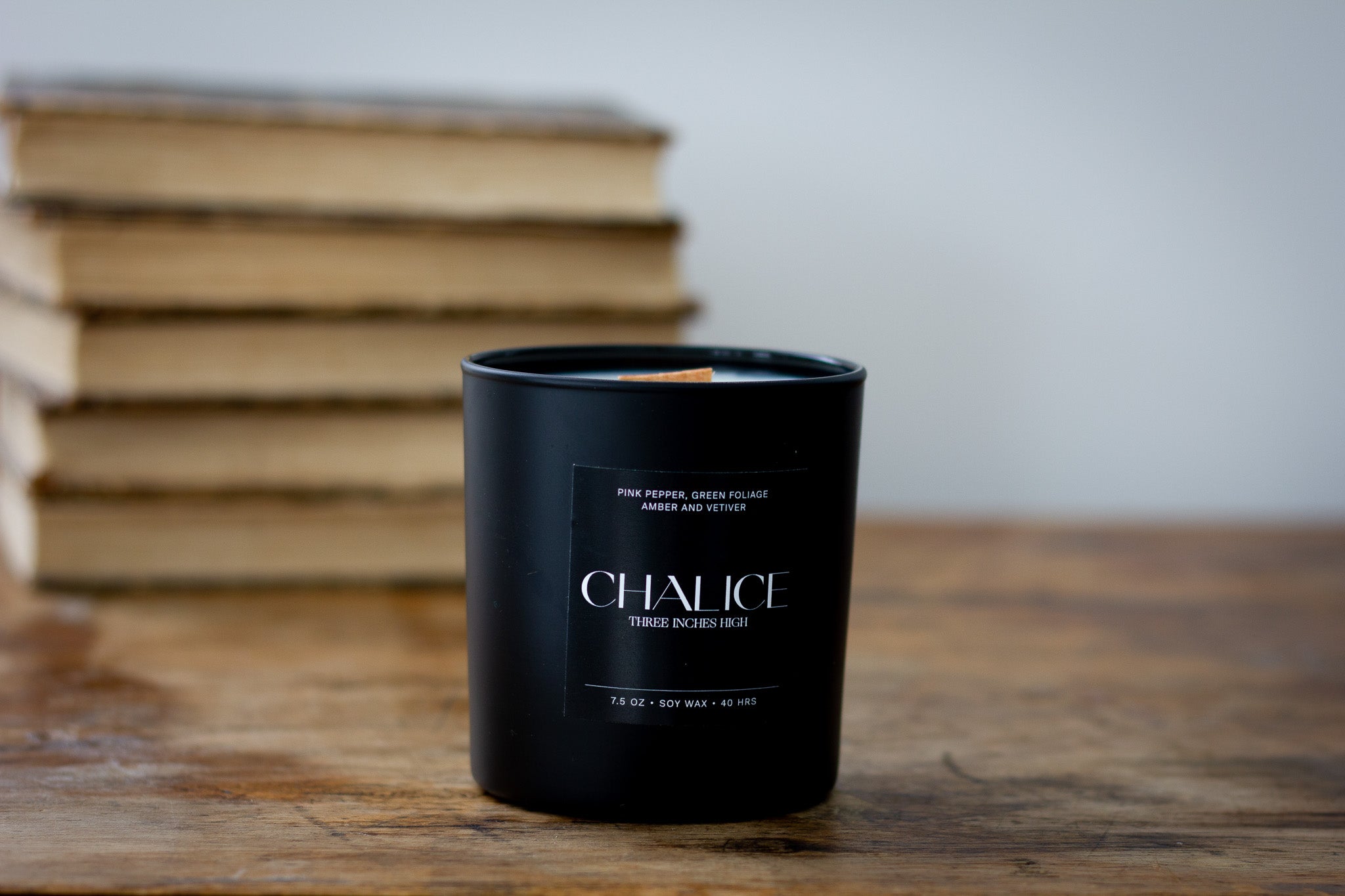 Black candle labeled 'Chalice' on a wooden surface with books in the background