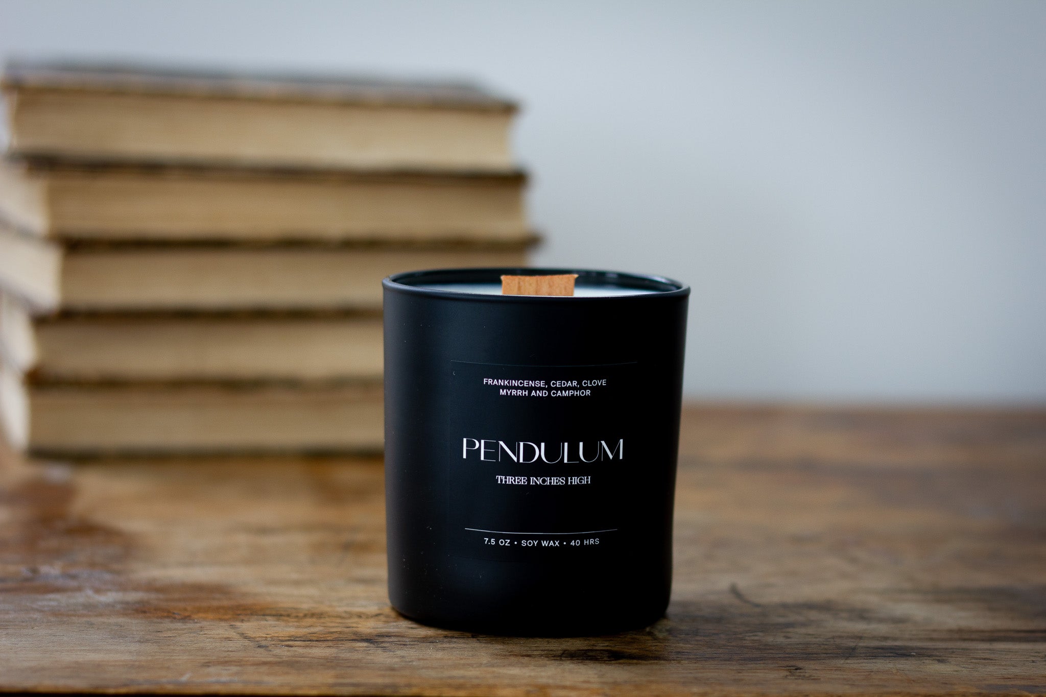 Black candle with 'Pendulum' branding on a wooden surface with books in the background