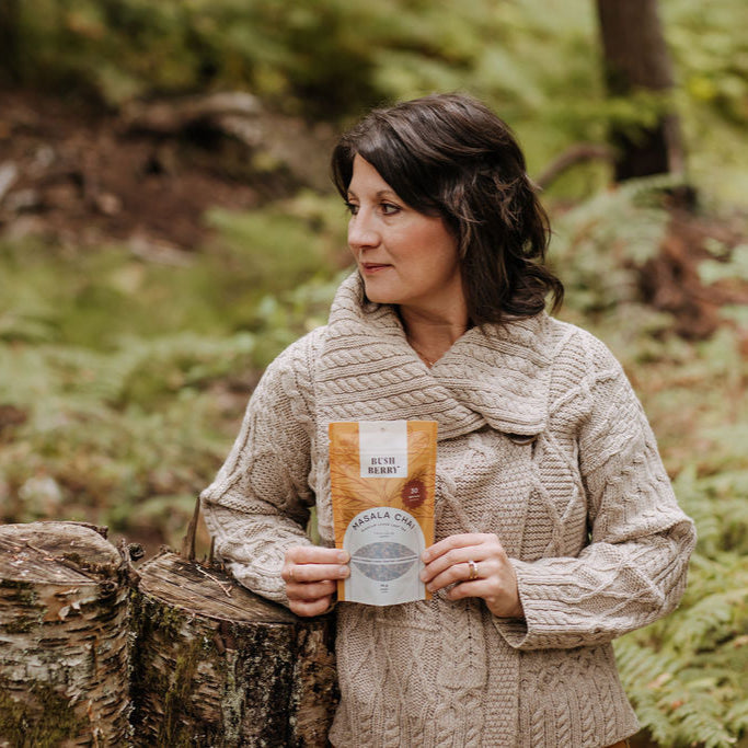 Woman holding a package of Bush Berry Organic Masala Chai Tea in a forest setting