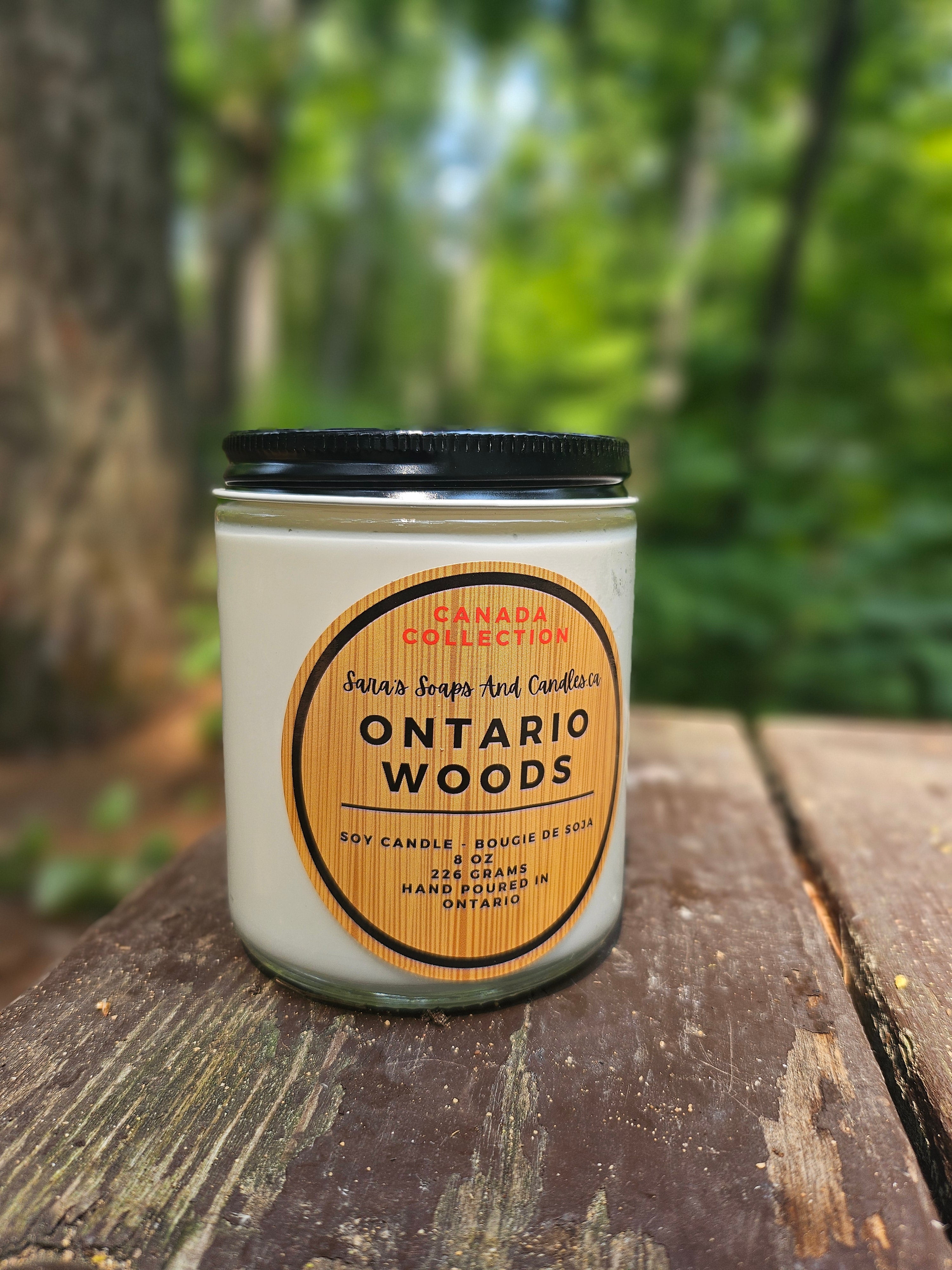 Candle labeled 'Ontario Woods' from the Canada Collection on a wooden surface with a forest background.