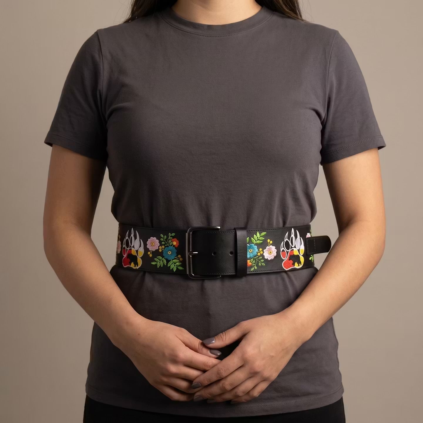 Person wearing a dark gray t-shirt with a decorative belt featuring floral and flame designs.