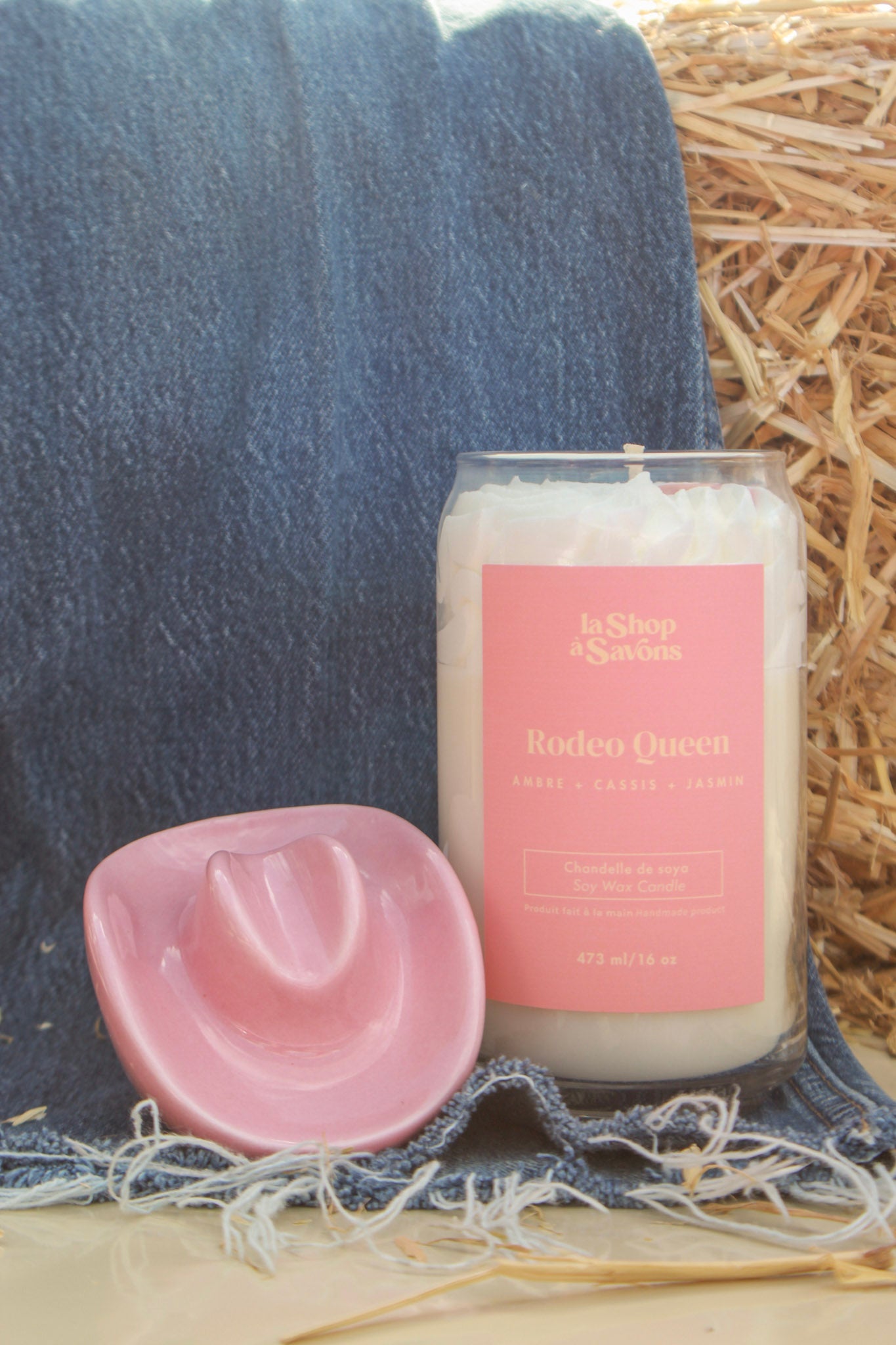 Candle labeled 'Rodeo Queen' with a pink cowboy hat on hay and denim background