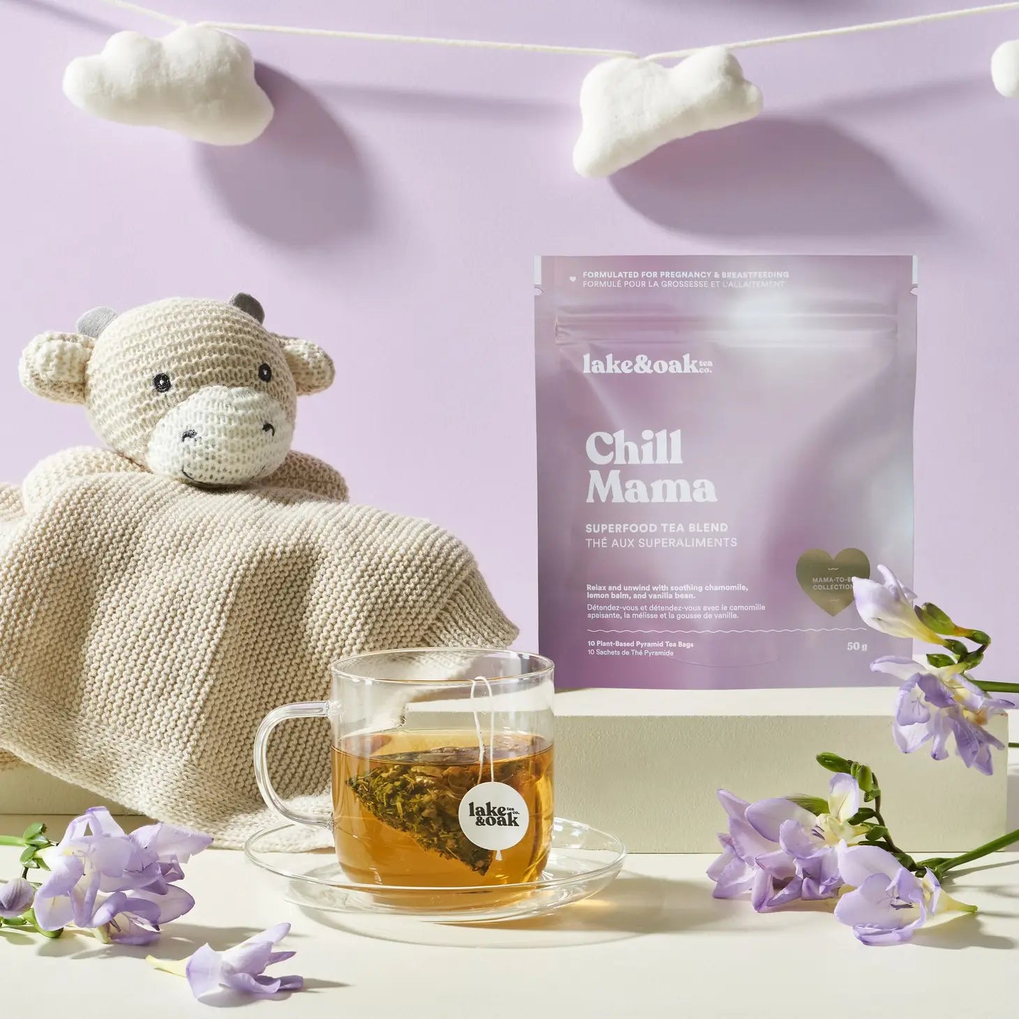 Chill Mama' by Lake & Oak superfood tea blend decaf with a cup of tea, knitted blanket, and toy on a light purple background.
