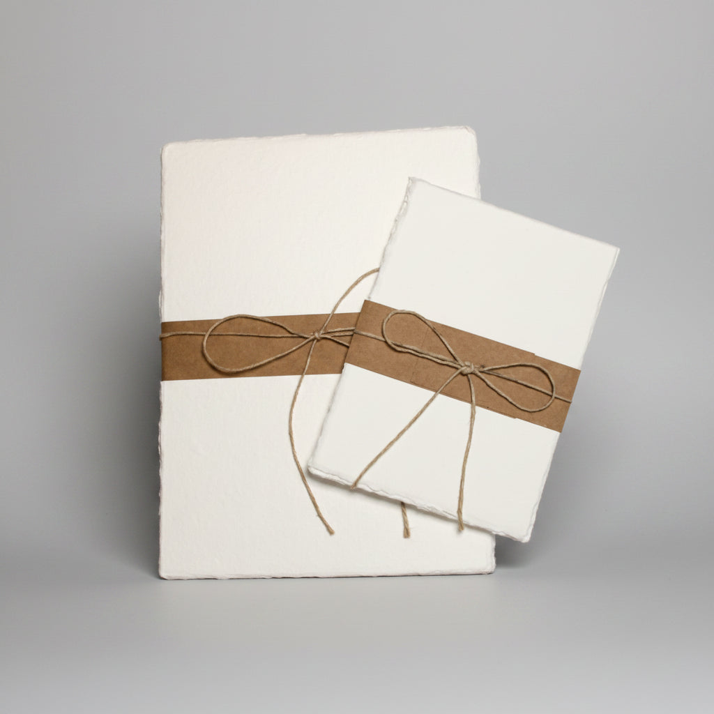 Two packs of handmade watercolor paper with brown ribbons on a white background