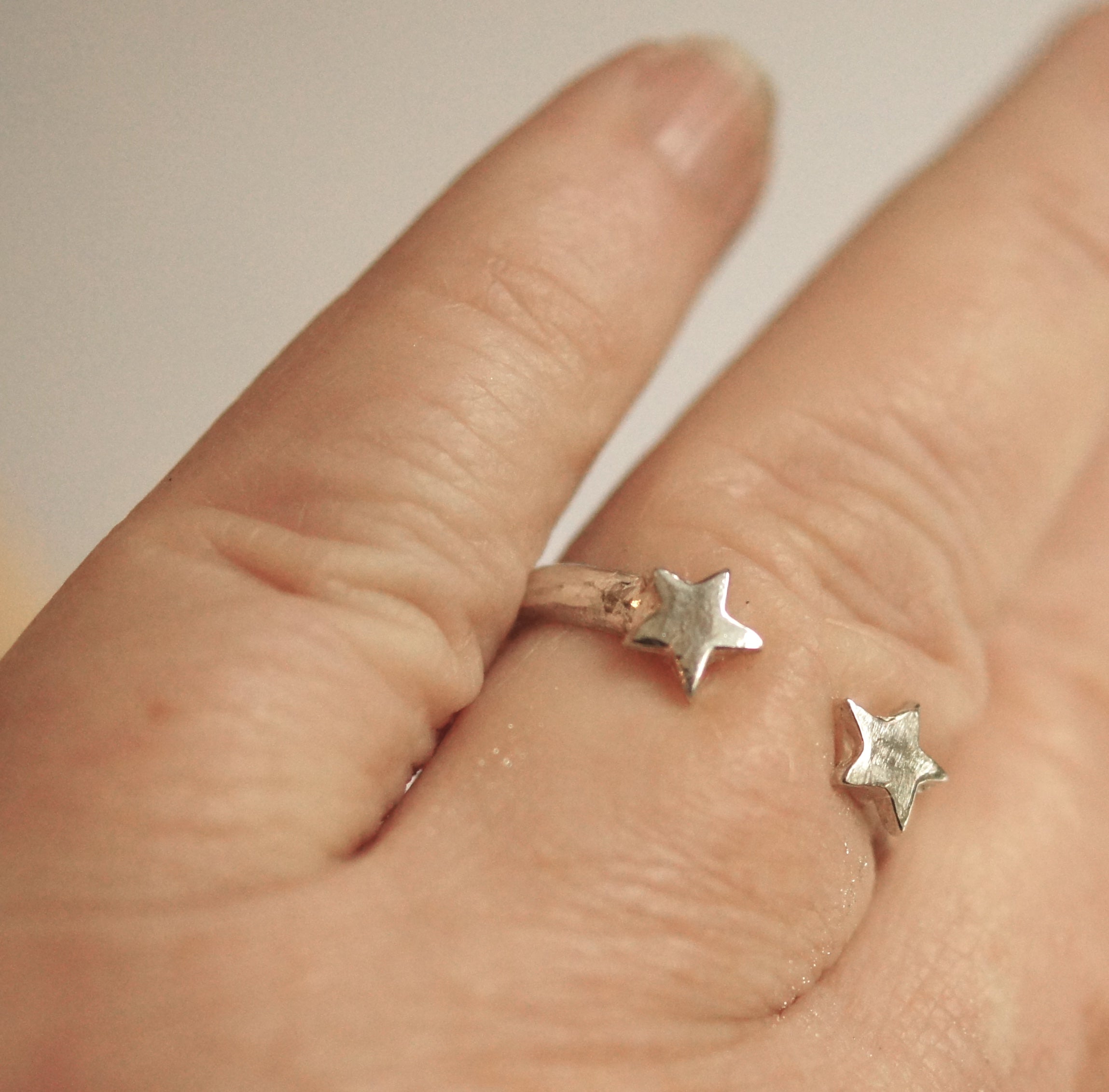 Silver star-shaped earrings on a hand with a neutral background