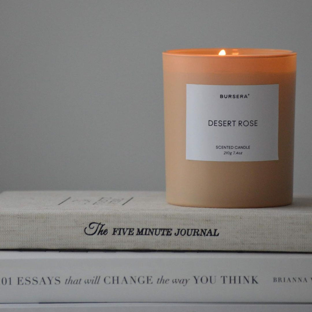 Candle labeled 'Desert Rose' on a stack of books with a gray background