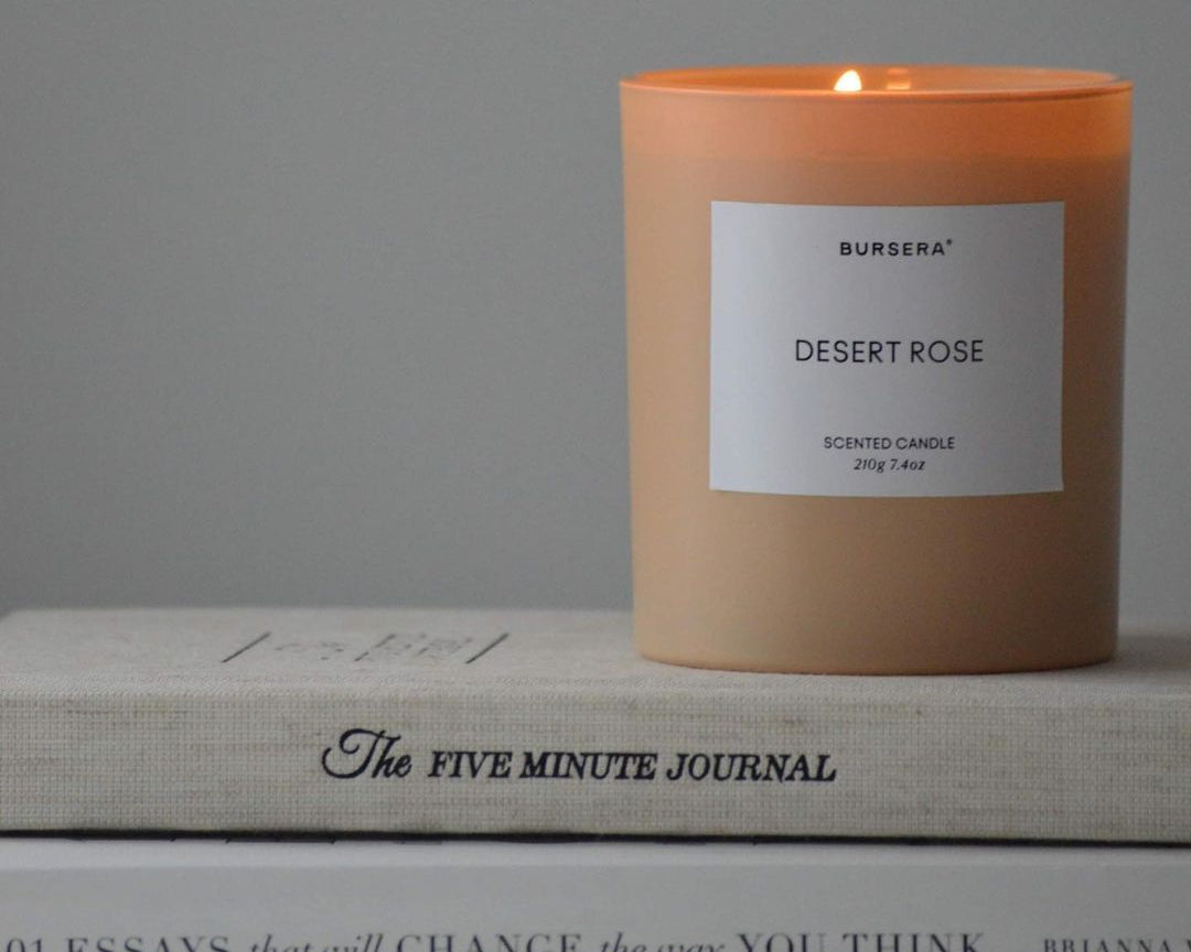 Candle labeled 'Desert Rose' on a stack of books with a gray background