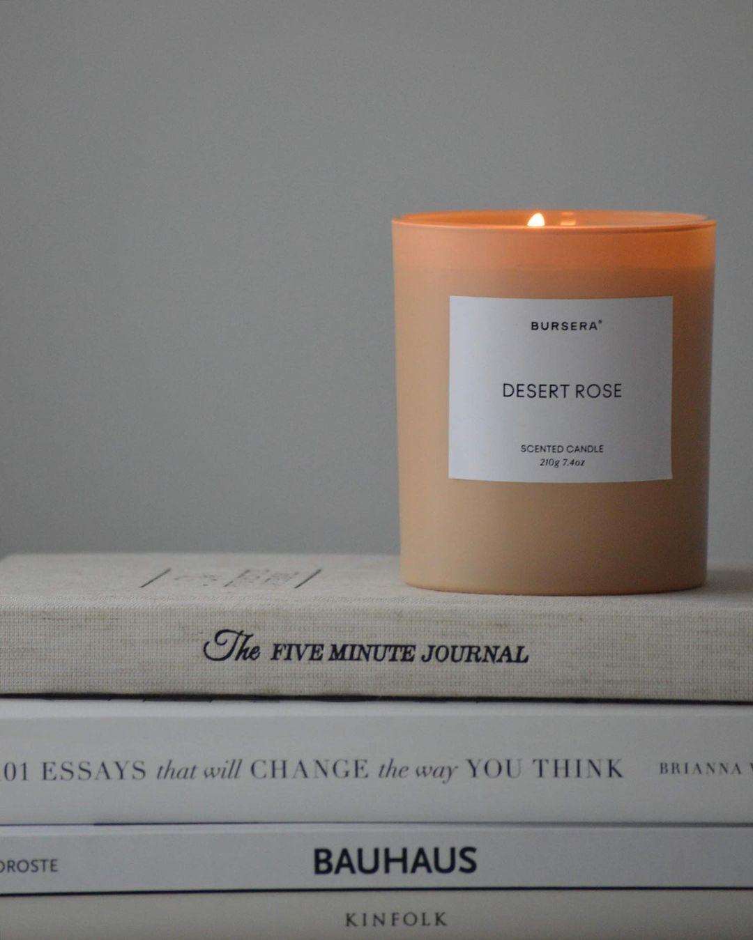 Candle labeled 'Desert Rose' on a stack of books with a gray background