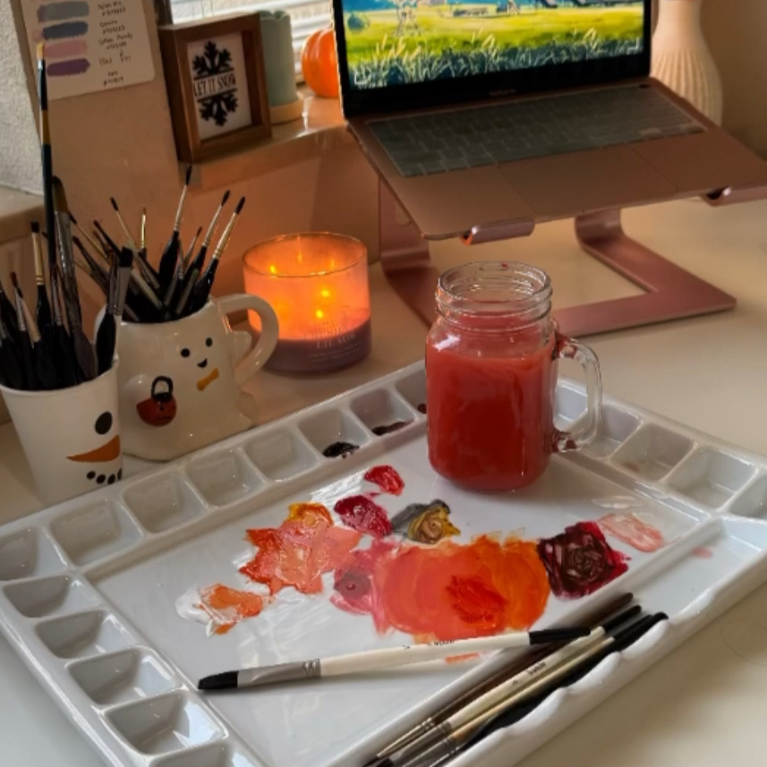 Artistic setup with laptop, paint palette, and art supplies on a desk.