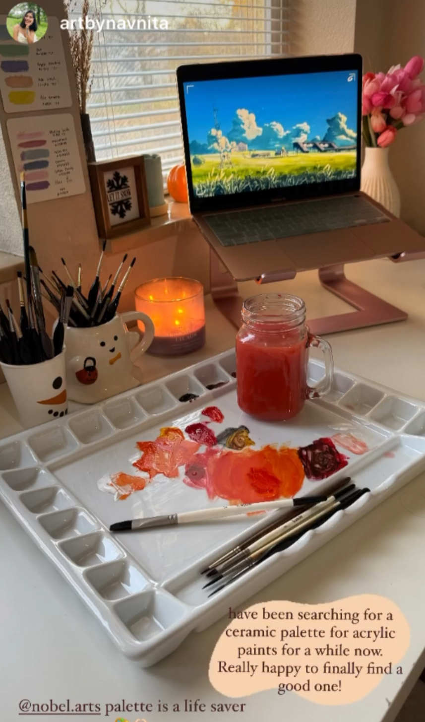 Artistic setup with laptop, paint palette, and art supplies on a desk.