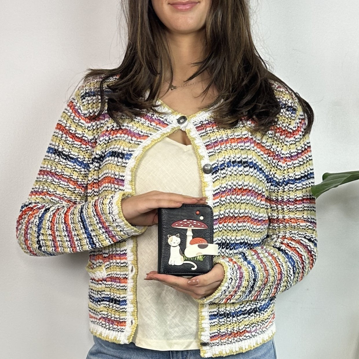 Person wearing a colorful striped jacket holding a Espe Vegan Corp small black bag with a cat design.